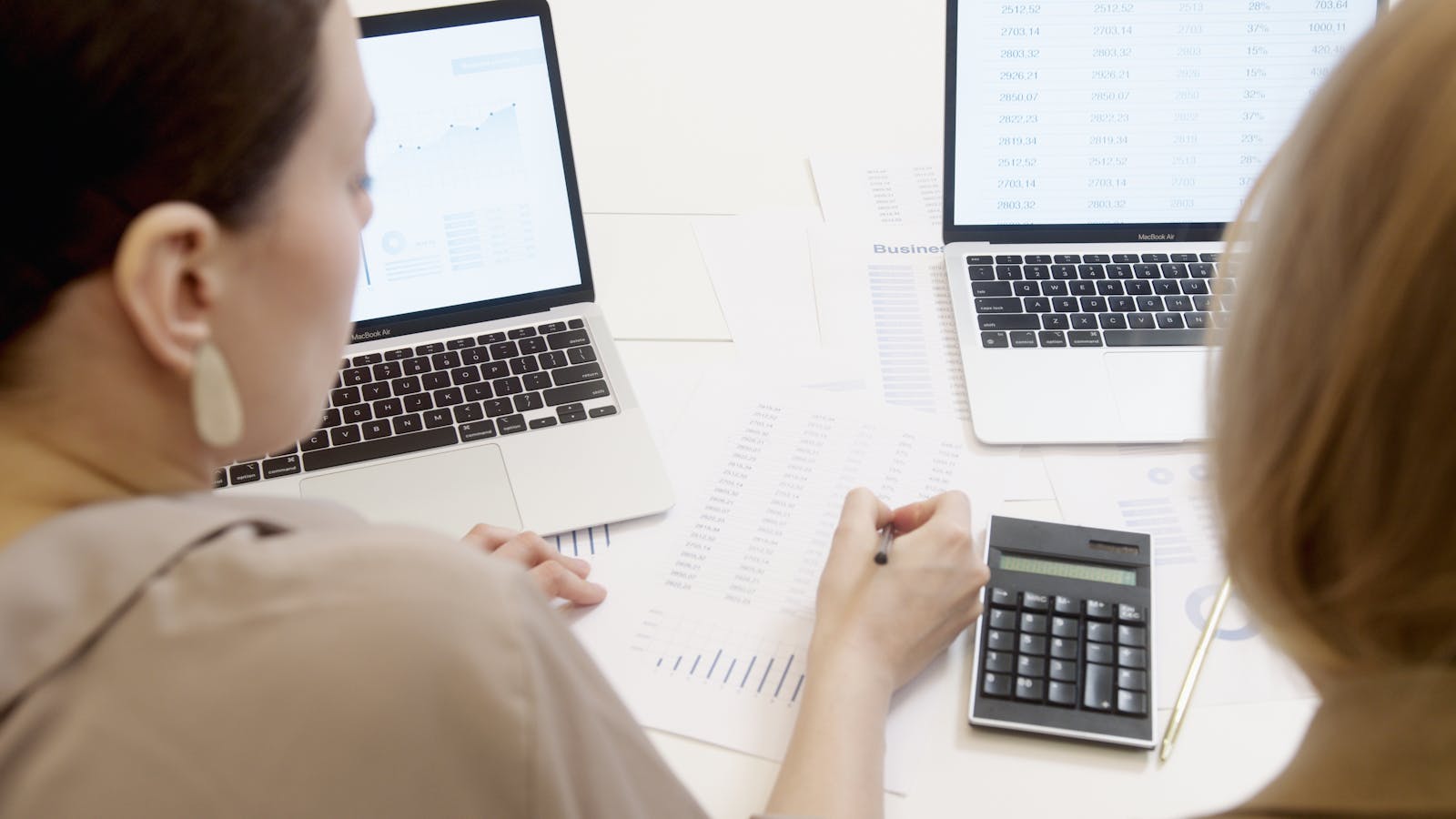 Two accountants reviewing spreadsheet data on laptops together