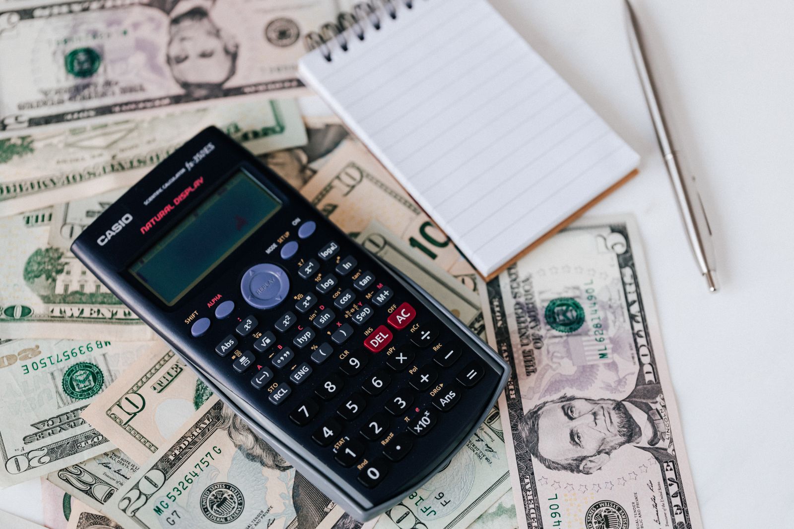 Calculator and notepad on top of dollar bills representing customer acquisition cost math