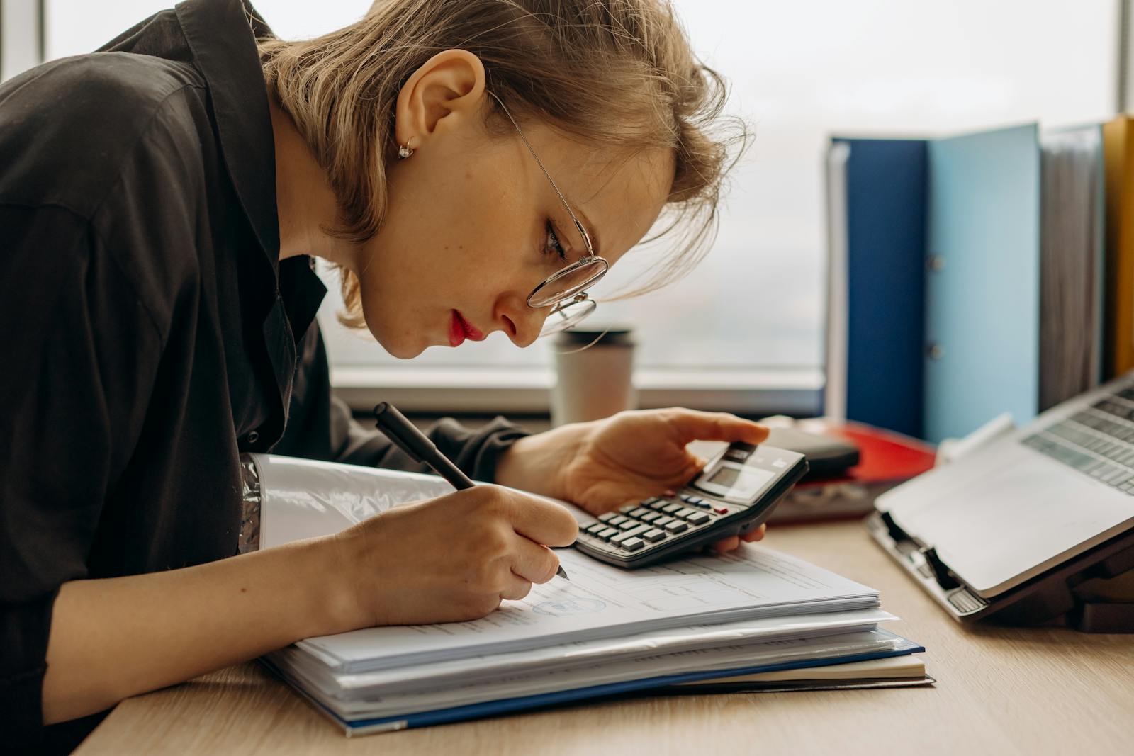 Accountant writing in a binder while using a calculator at her desk