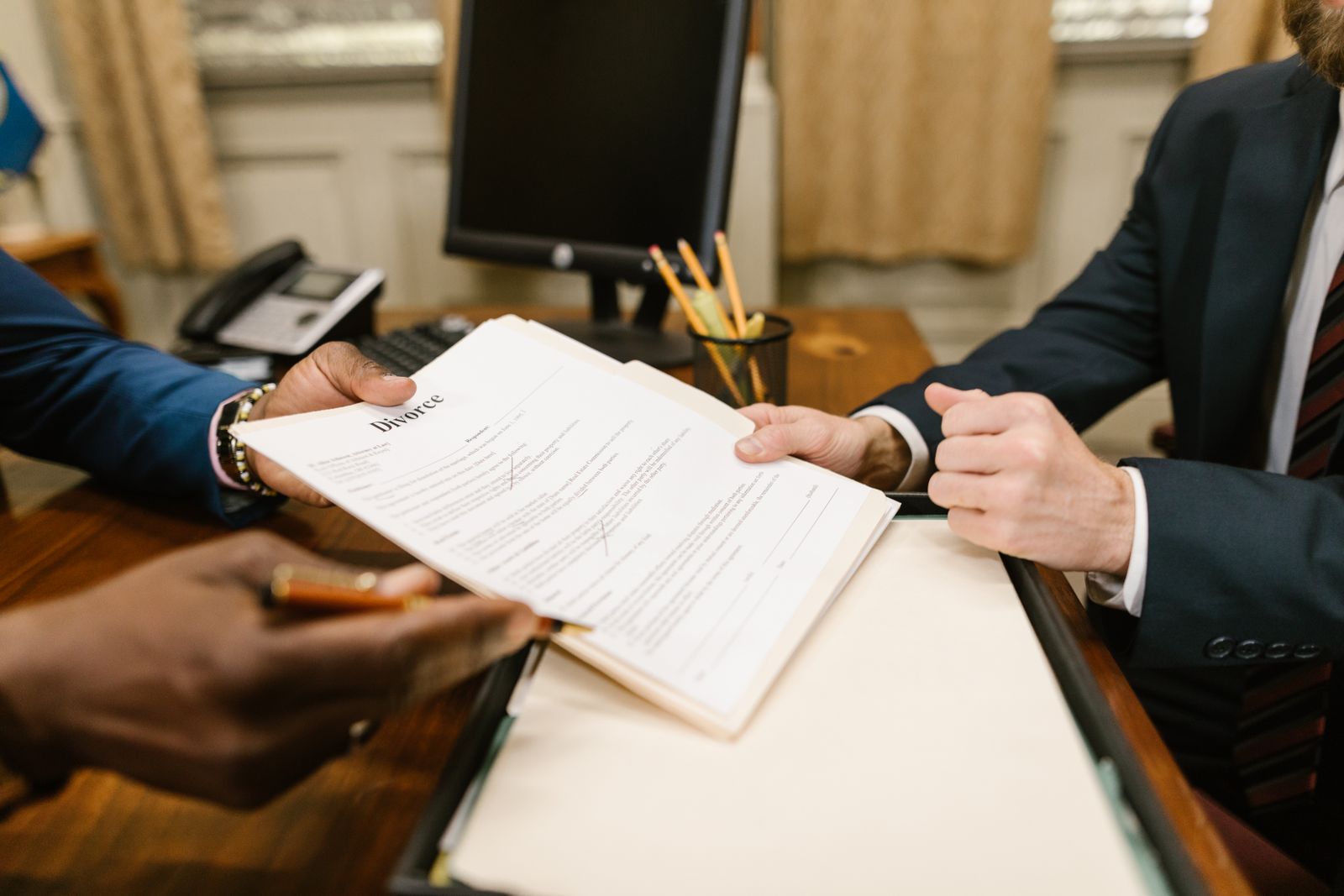 Close-up of hands exchanging divorce paperwork across an attorney's desk