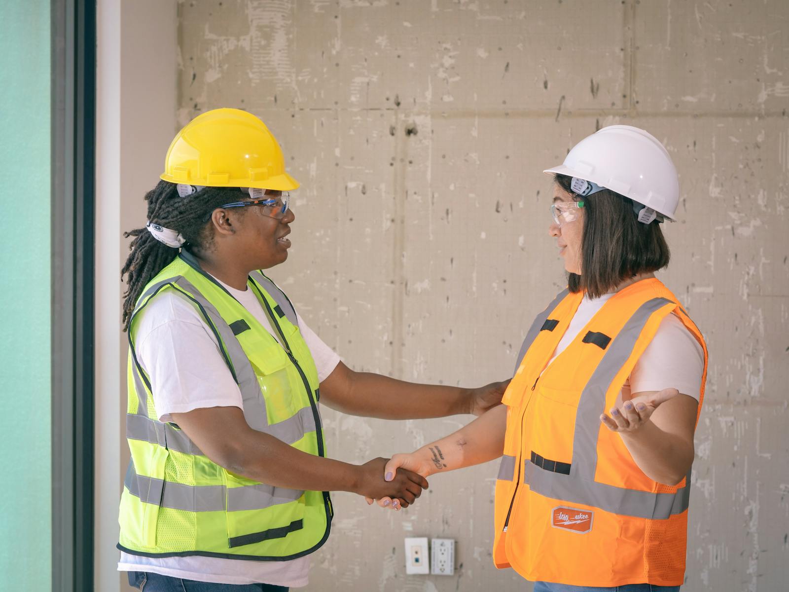 Two contractors in safety gear shaking hands after closing a job