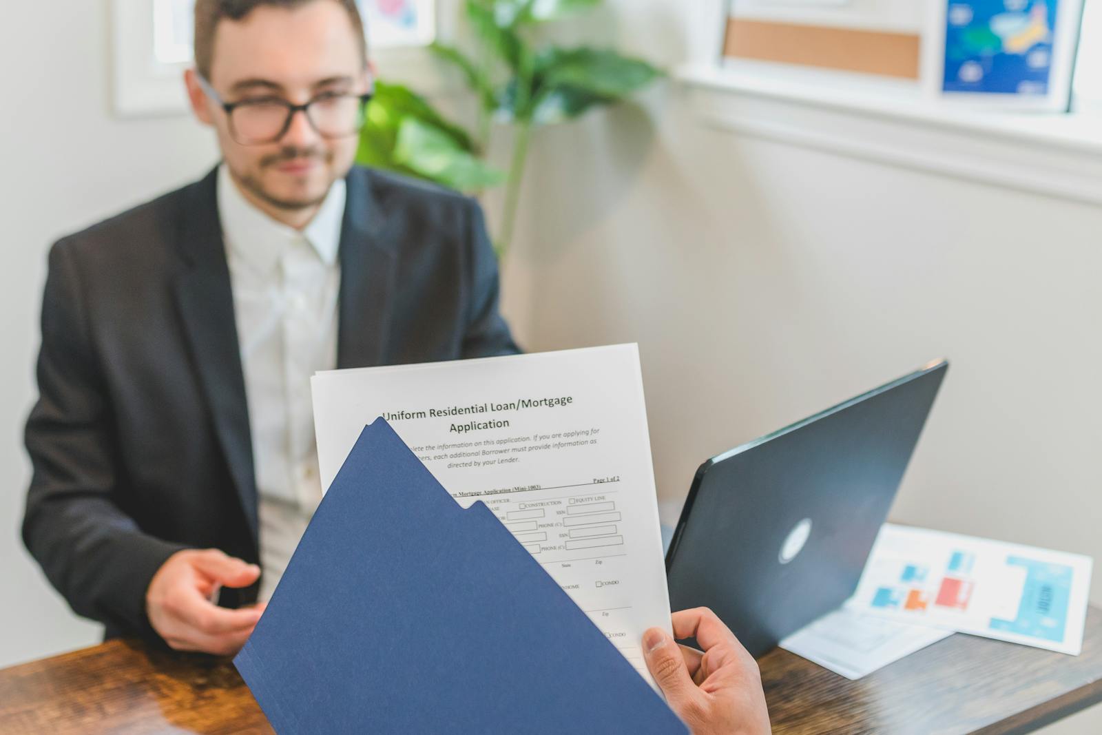 Mortgage broker reviewing loan application documents with a client at a desk