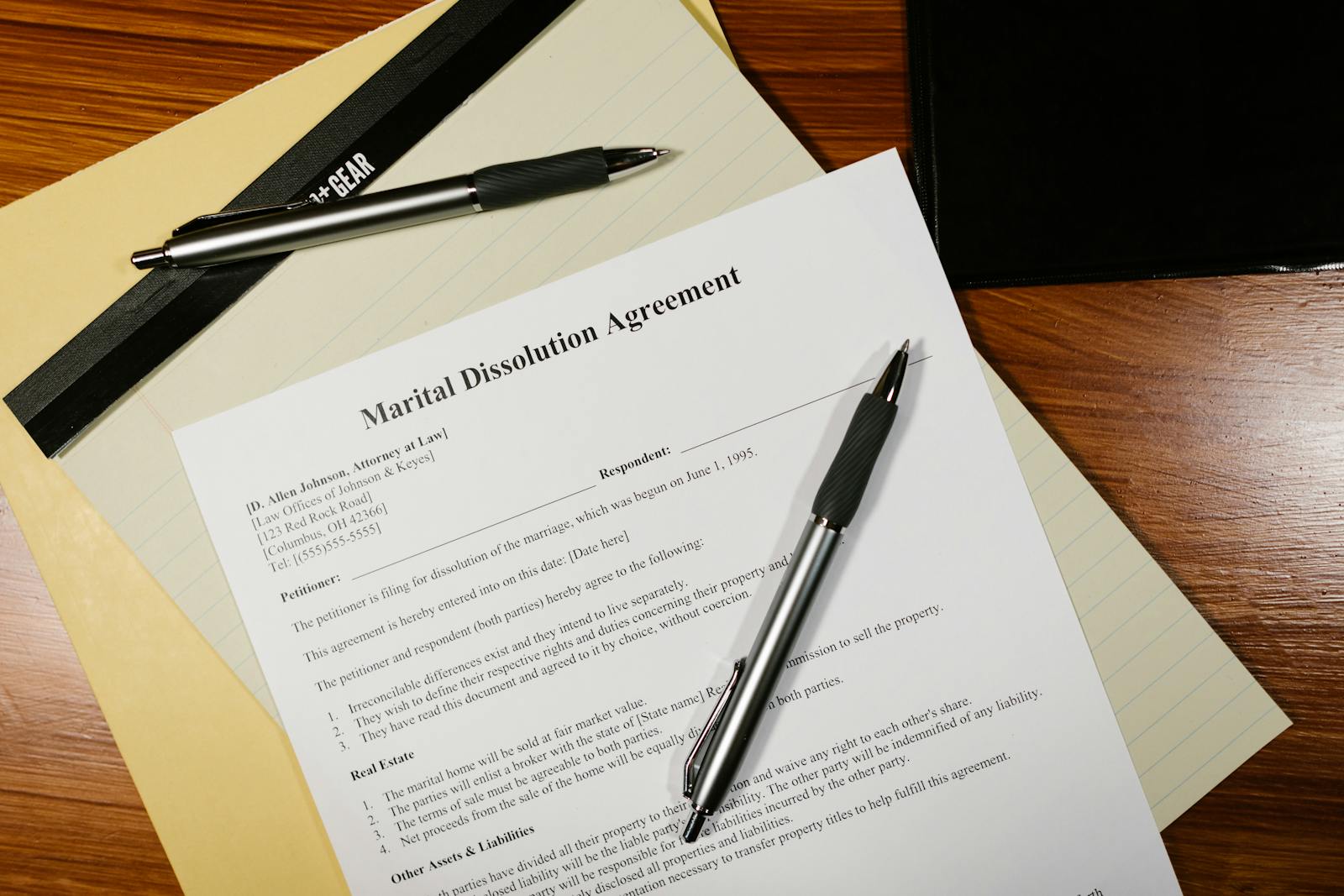 Marital dissolution agreement paperwork laid out on a wooden desk with pens