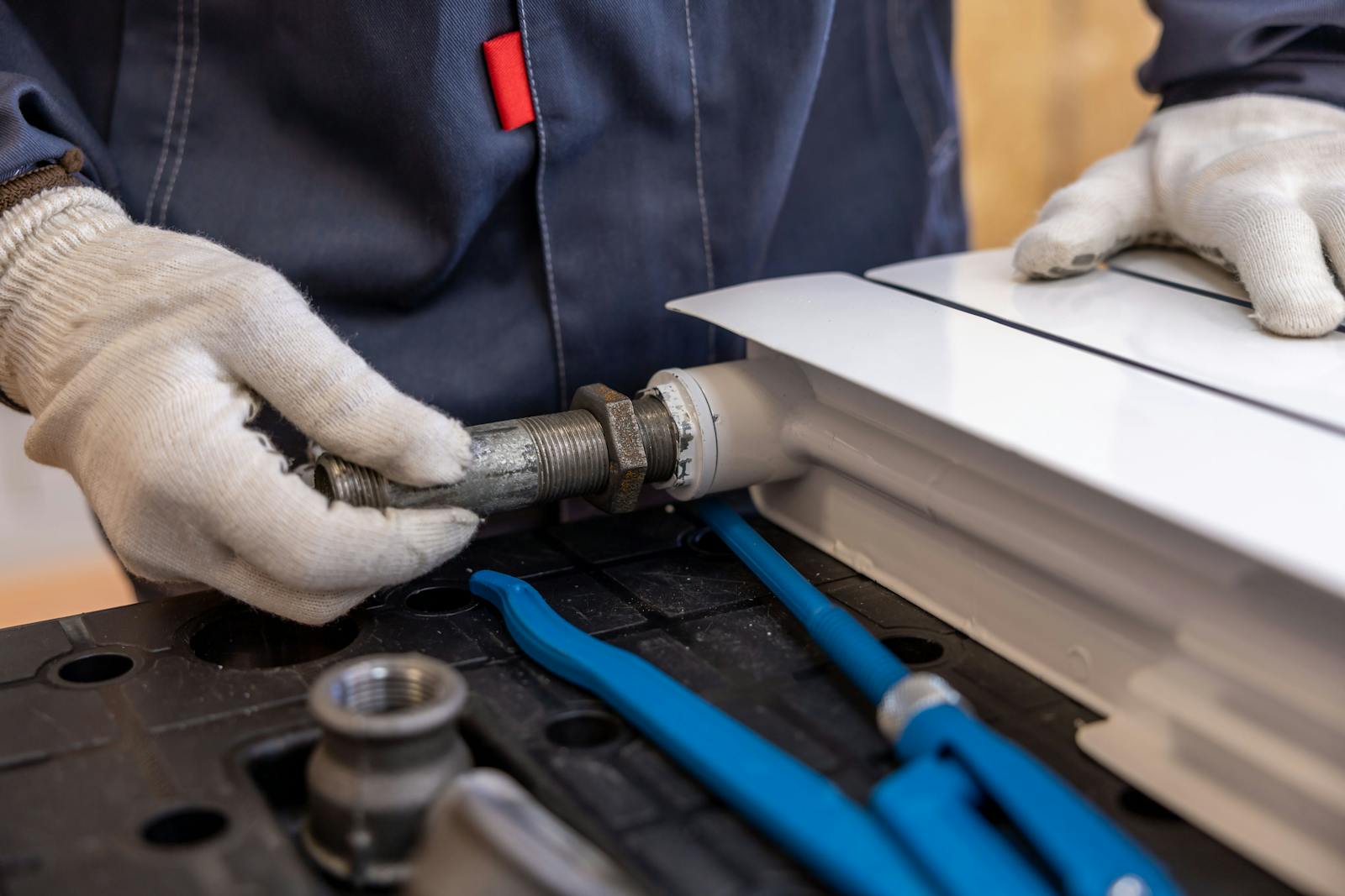 Close-up of a plumber's gloved hands installing a radiator pipe
