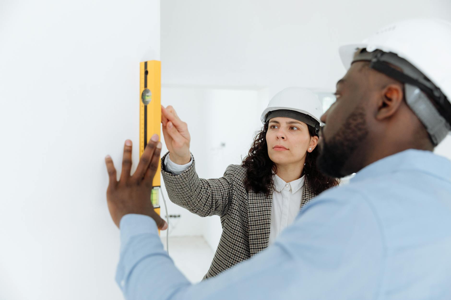 Two contractors using a level tool on a wall indoors.