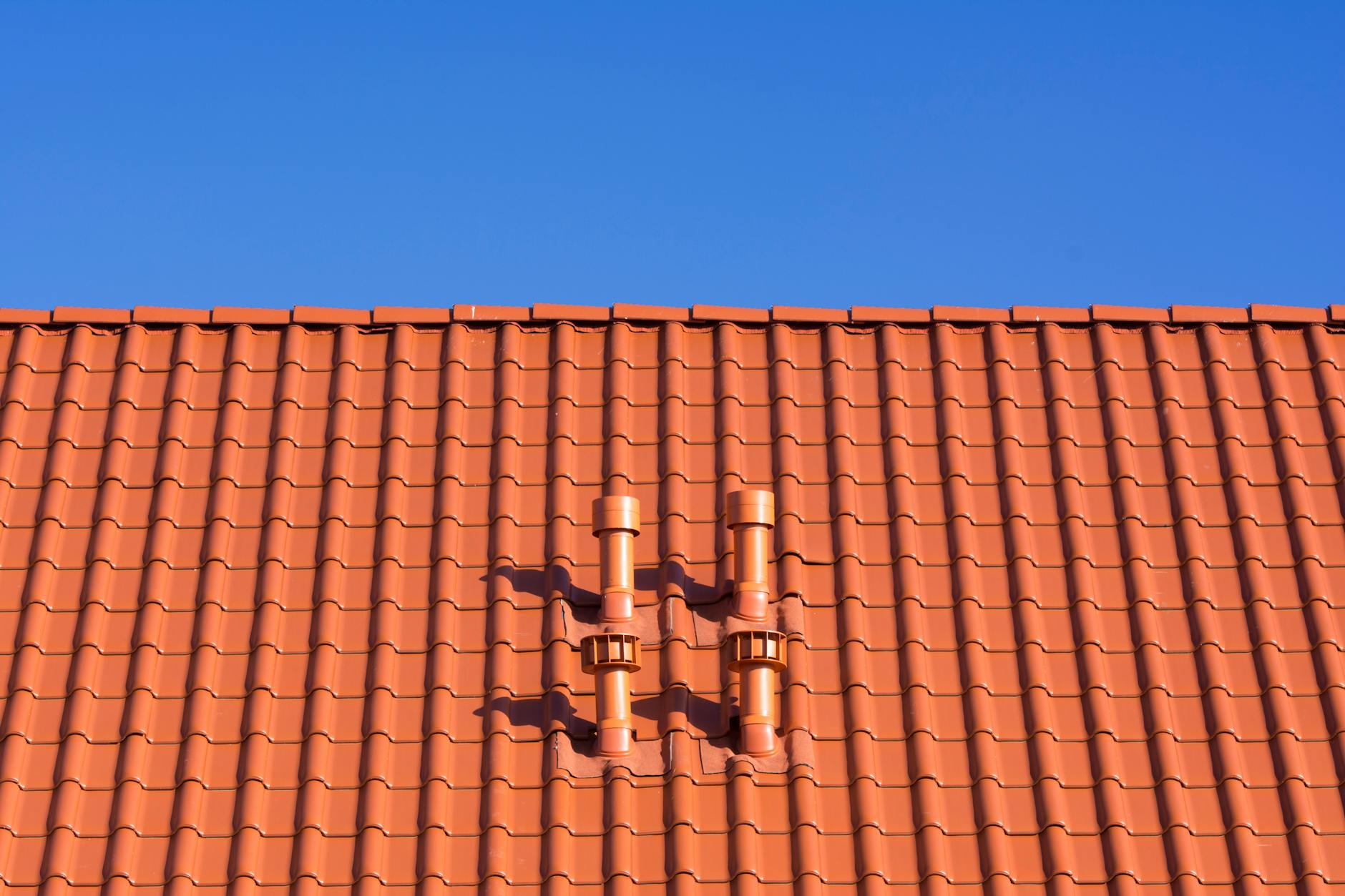 Close up of tile roof with vent stacks against blue sky
