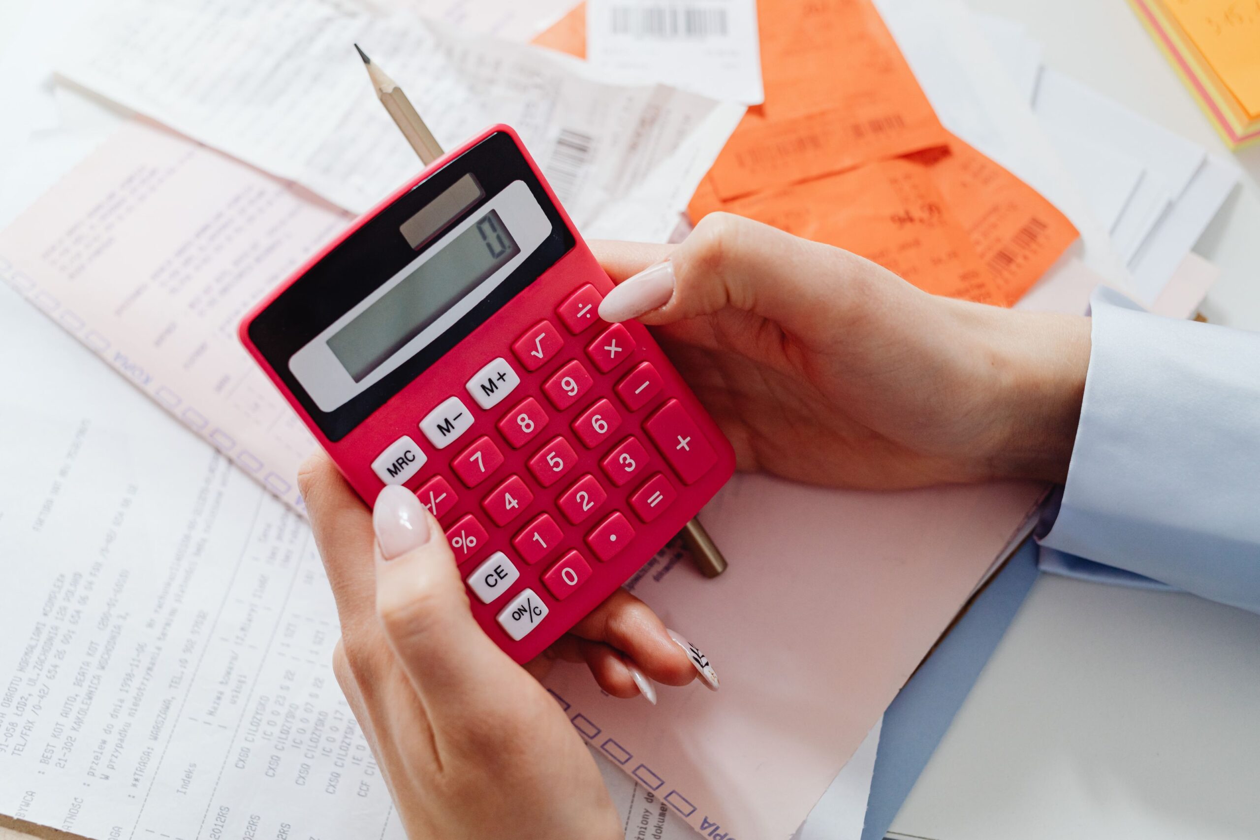 Hand using a calculator over receipts and invoices to compare accounting marketing costs