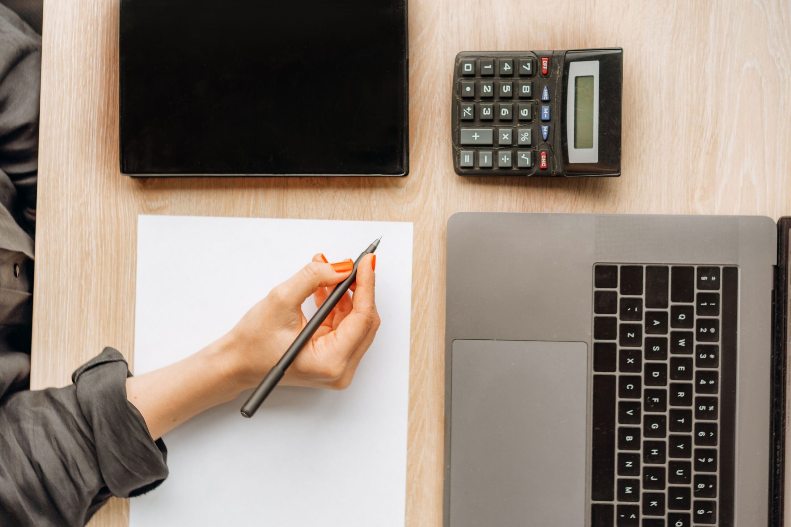 Person calculating costs at an office desk with a laptop, tablet and calculator