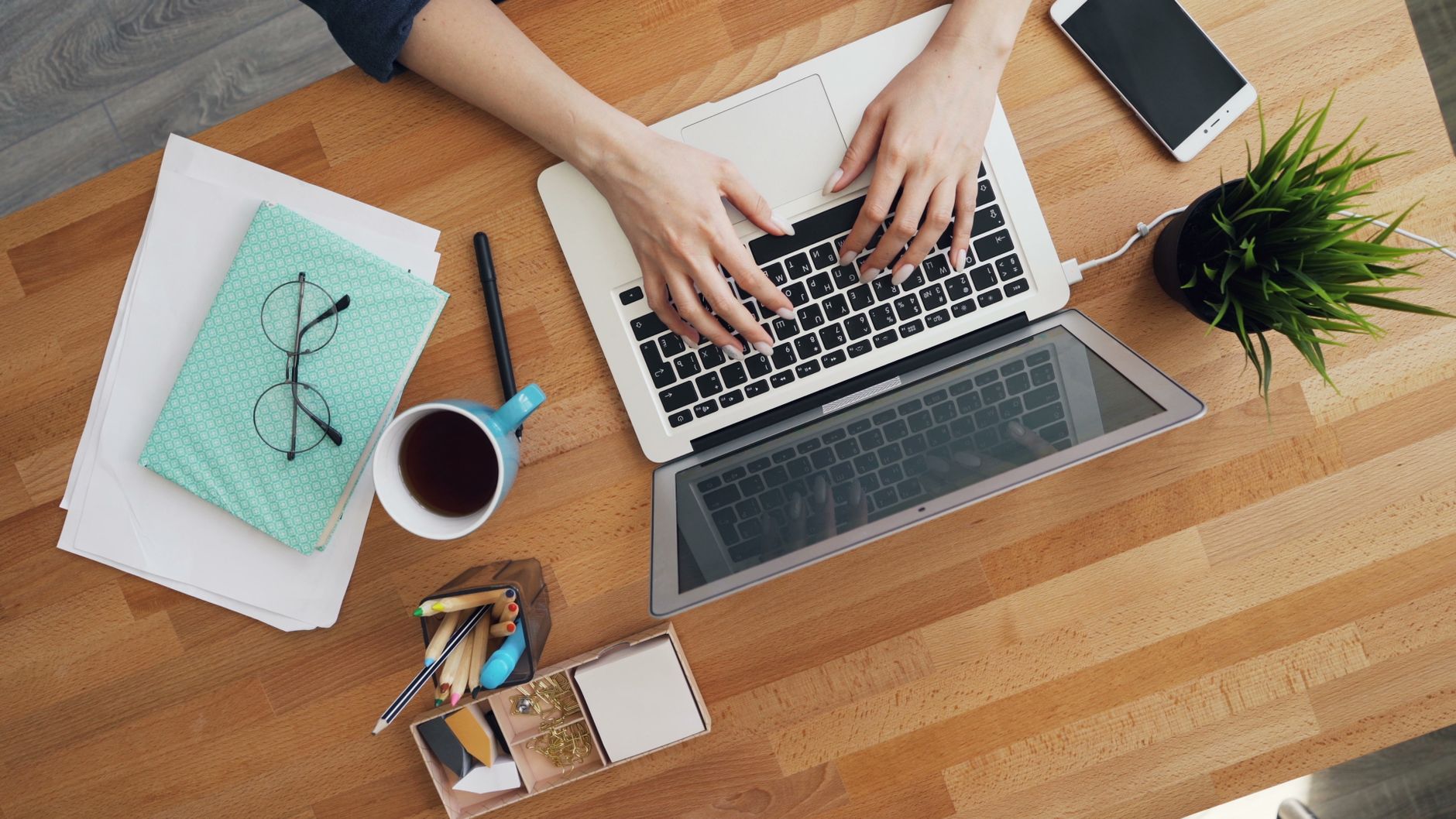 Overhead view of hands typing a blog post on a laptop with coffee and a notebook