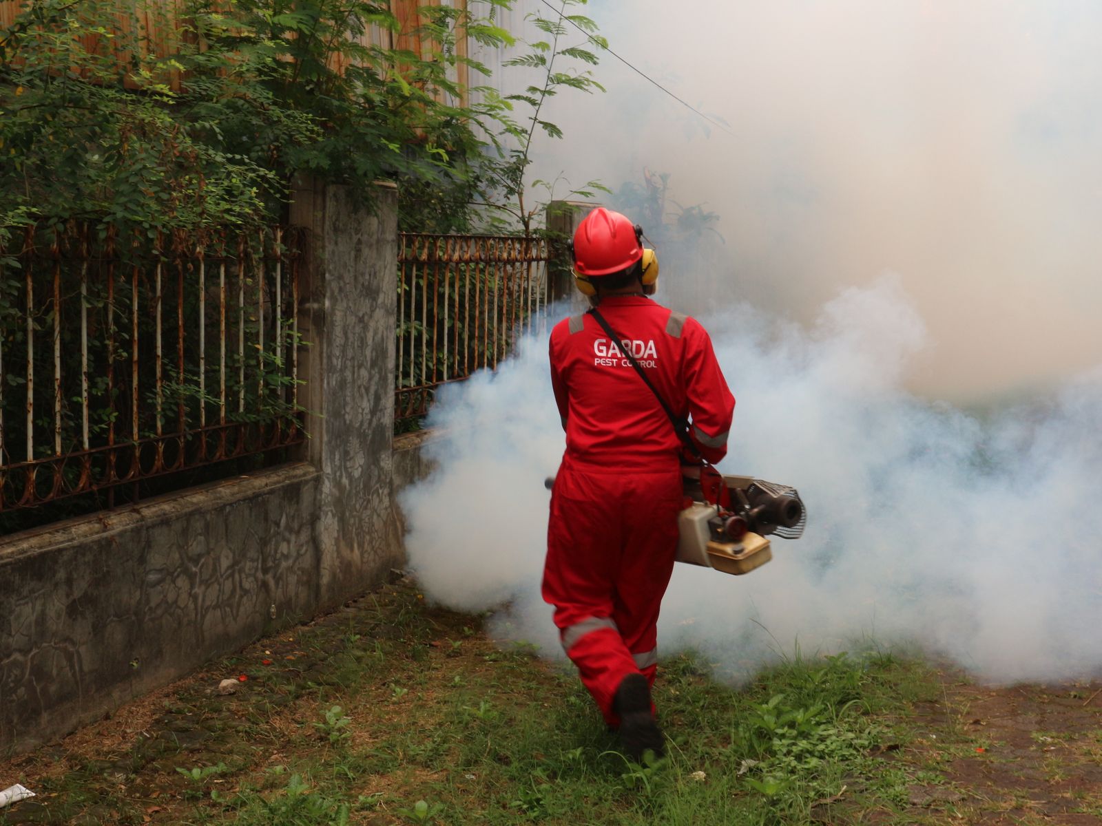 Uniformed pest control company technician with branded coveralls fogging a property