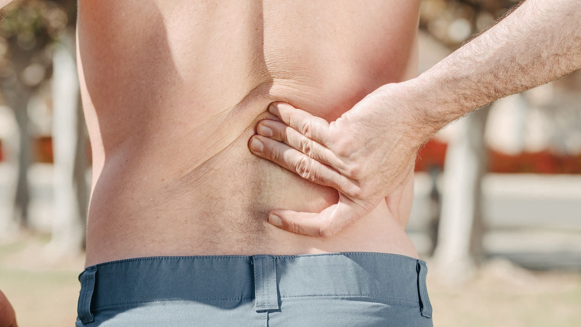 Close-up of a man gripping his lower back in pain outdoors, typical of patients searching Google for chiropractic relief