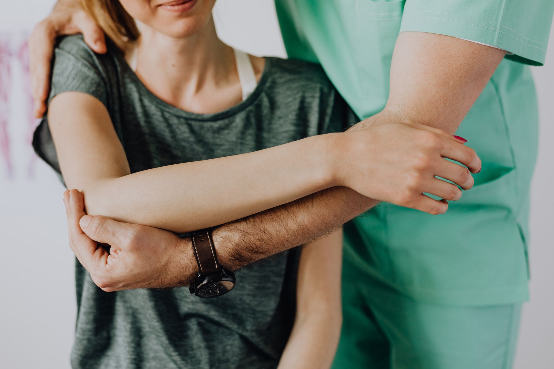 Chiropractor in green scrubs stretching a patient's arm during a clinical treatment session