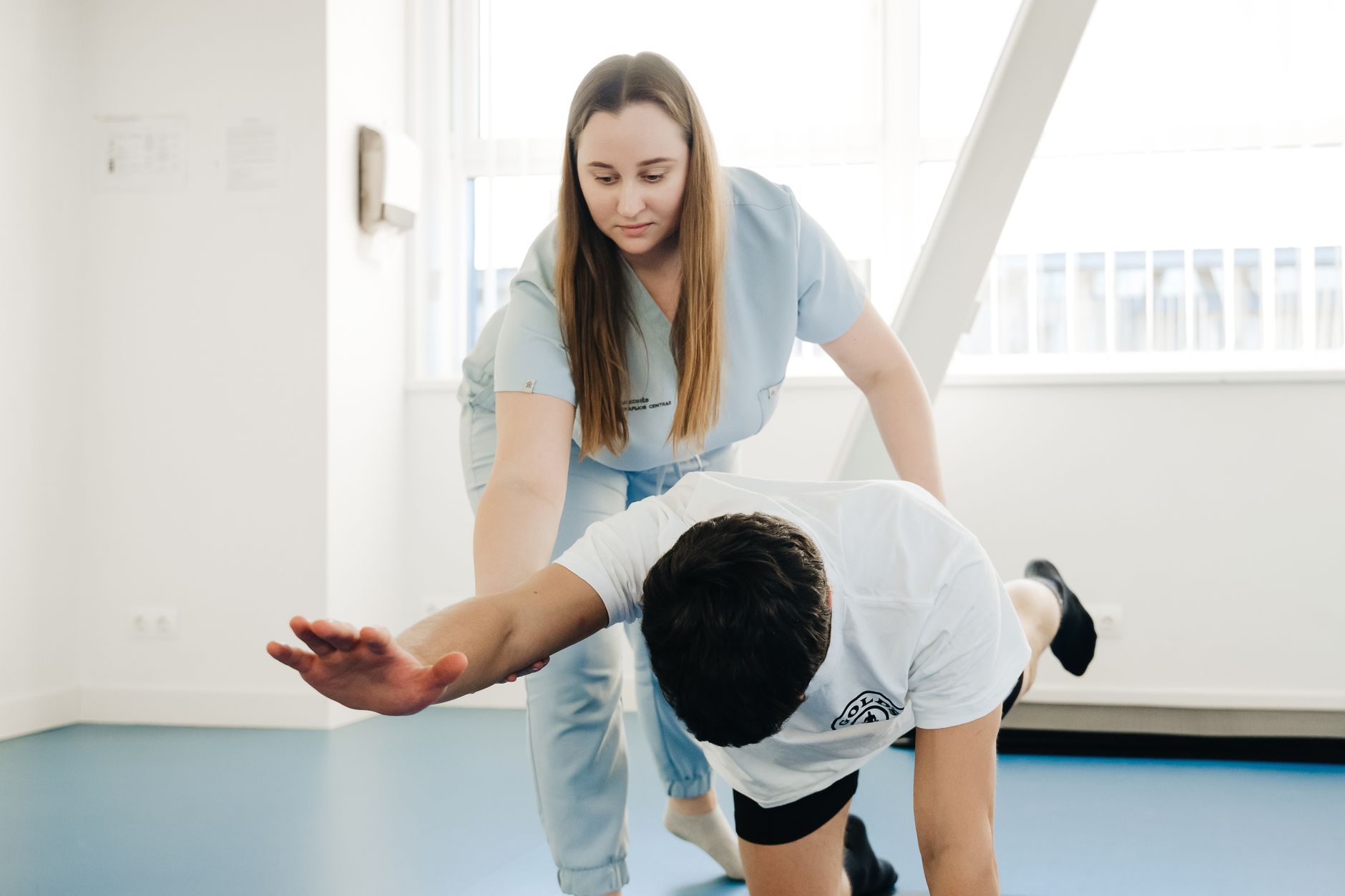 Chiropractic assistant guiding a male patient through stretching exercises in a bright physical therapy room
