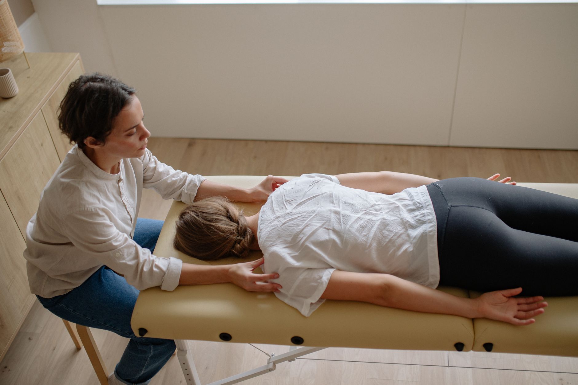 Chiropractor performing a back adjustment on a patient lying face-down on a treatment table in a bright clinic