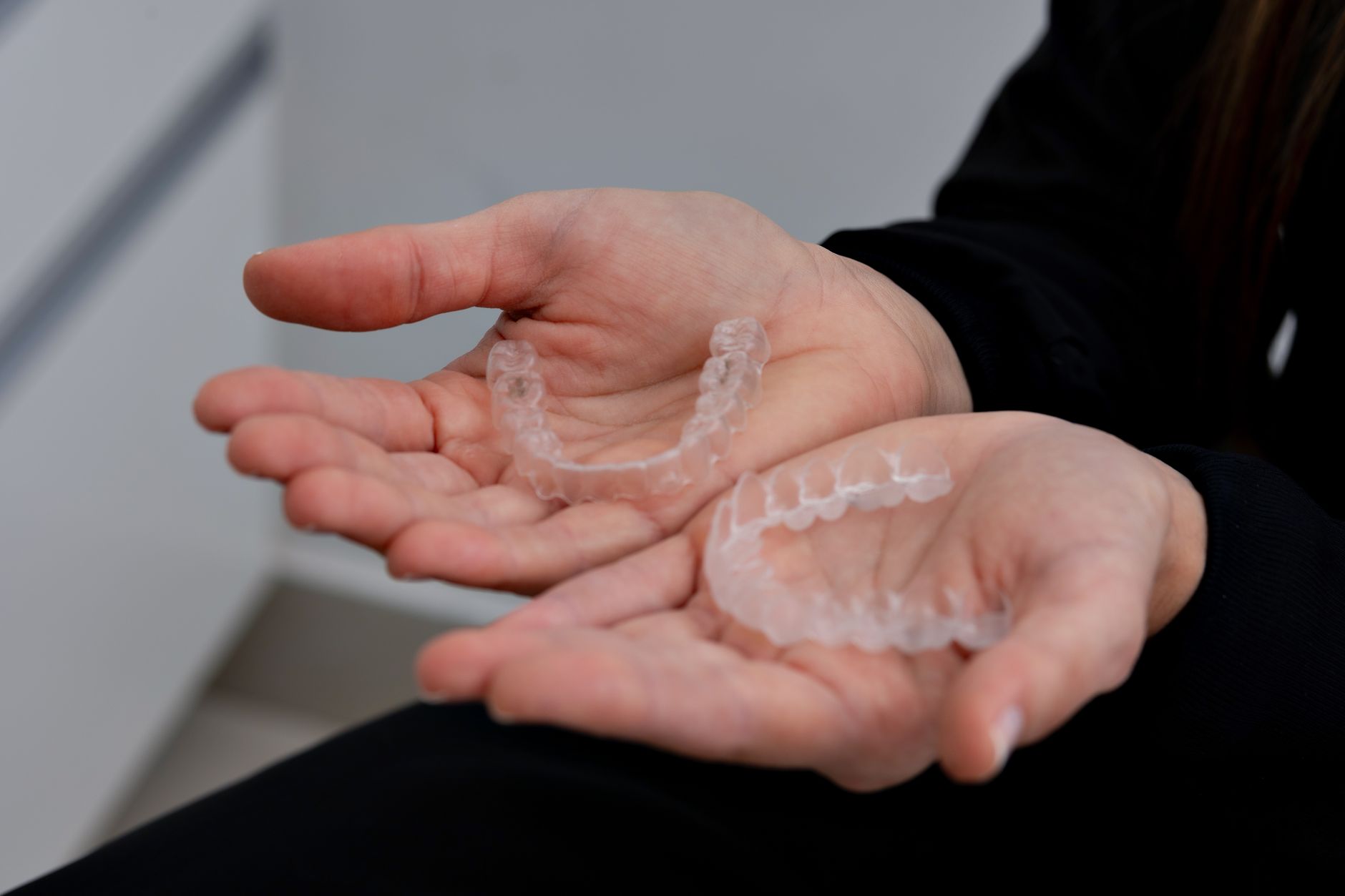 Clear Invisalign aligners held up at a modern cosmetic dental office