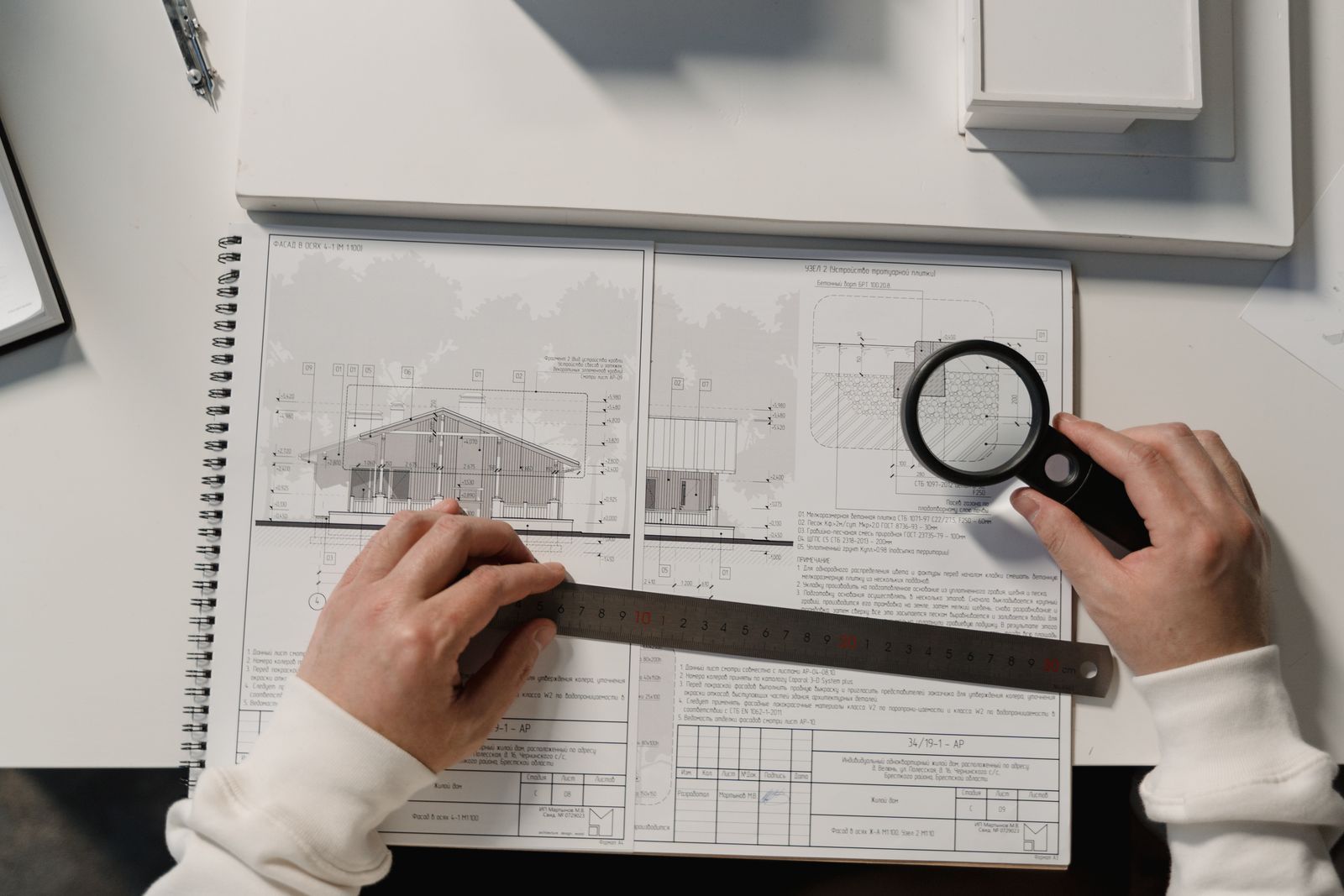 Architect measuring concrete project blueprints with a metal ruler and magnifying glass