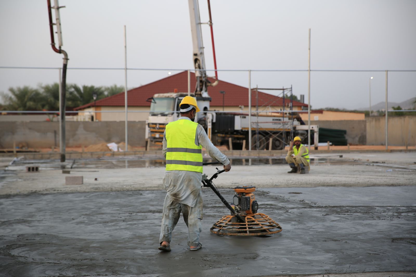 Concrete finisher using a power trowel to smooth a freshly poured slab at dusk
