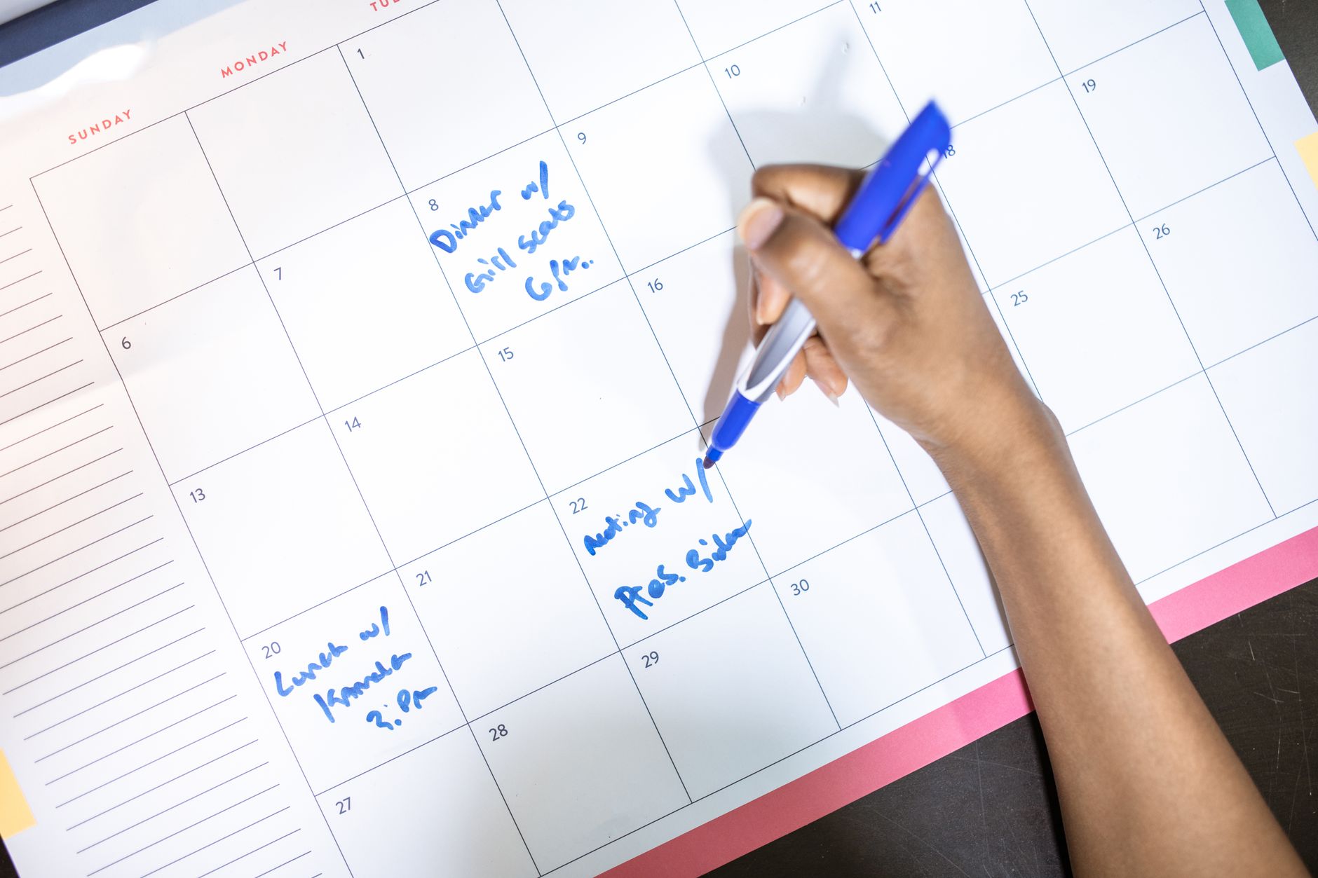 Hand writing scheduled content publishing dates on a desk calendar with blue pen