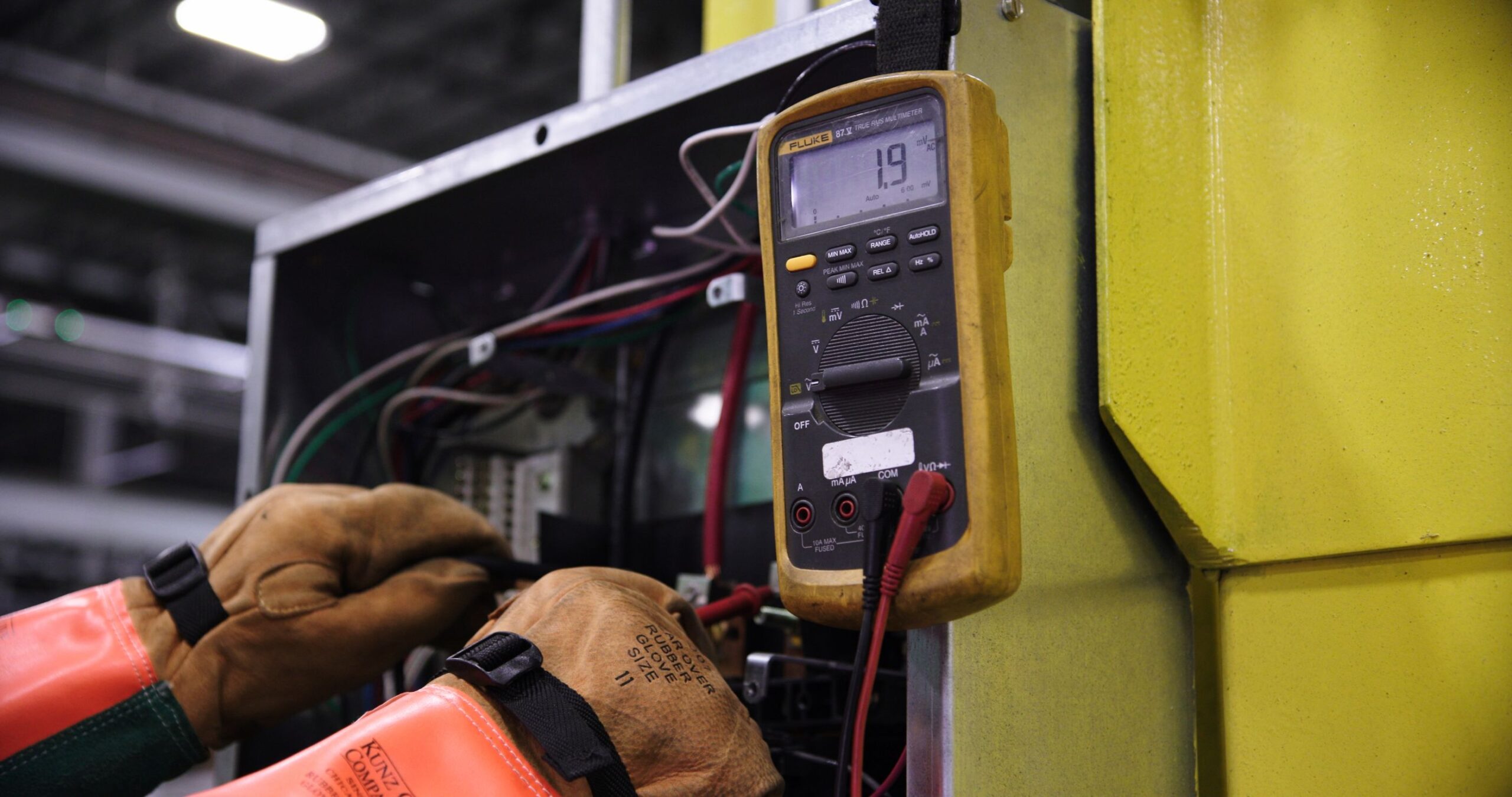 Electrician using a digital multimeter to test voltage in a control panel during a diagnostic