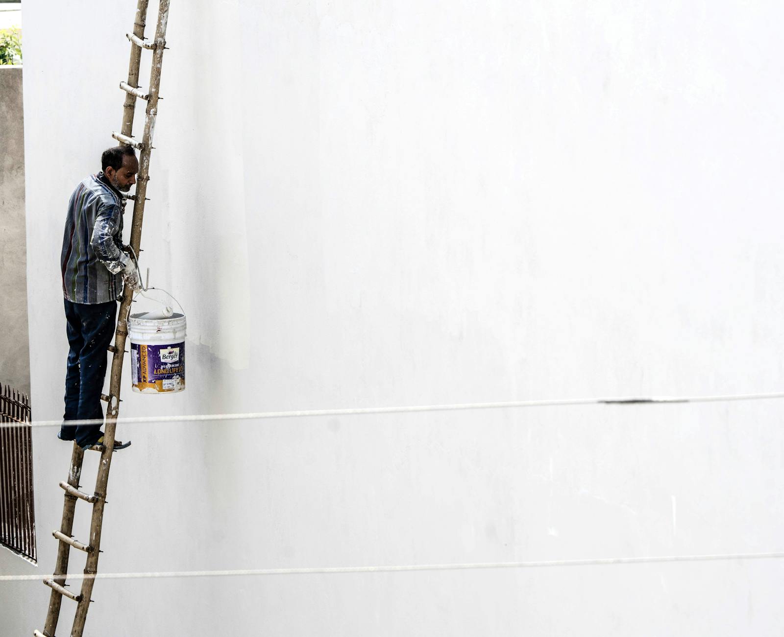 Professional painter on a ladder applying paint to a tall exterior wall on a residential job