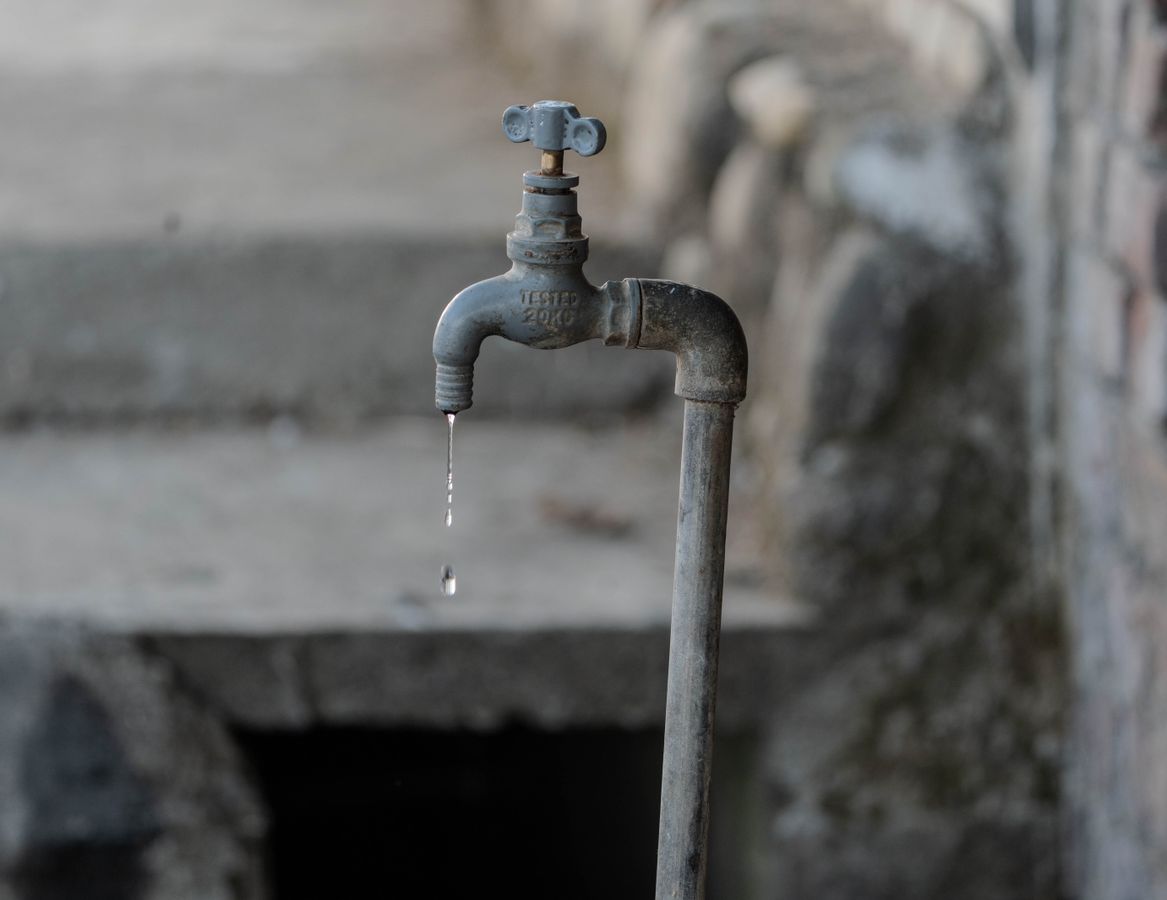An old metal outdoor faucet dripping water against a stone wall