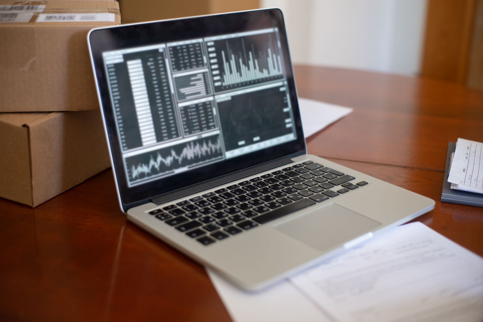 Laptop displaying analytics dashboards on wooden desk beside shipping boxes
