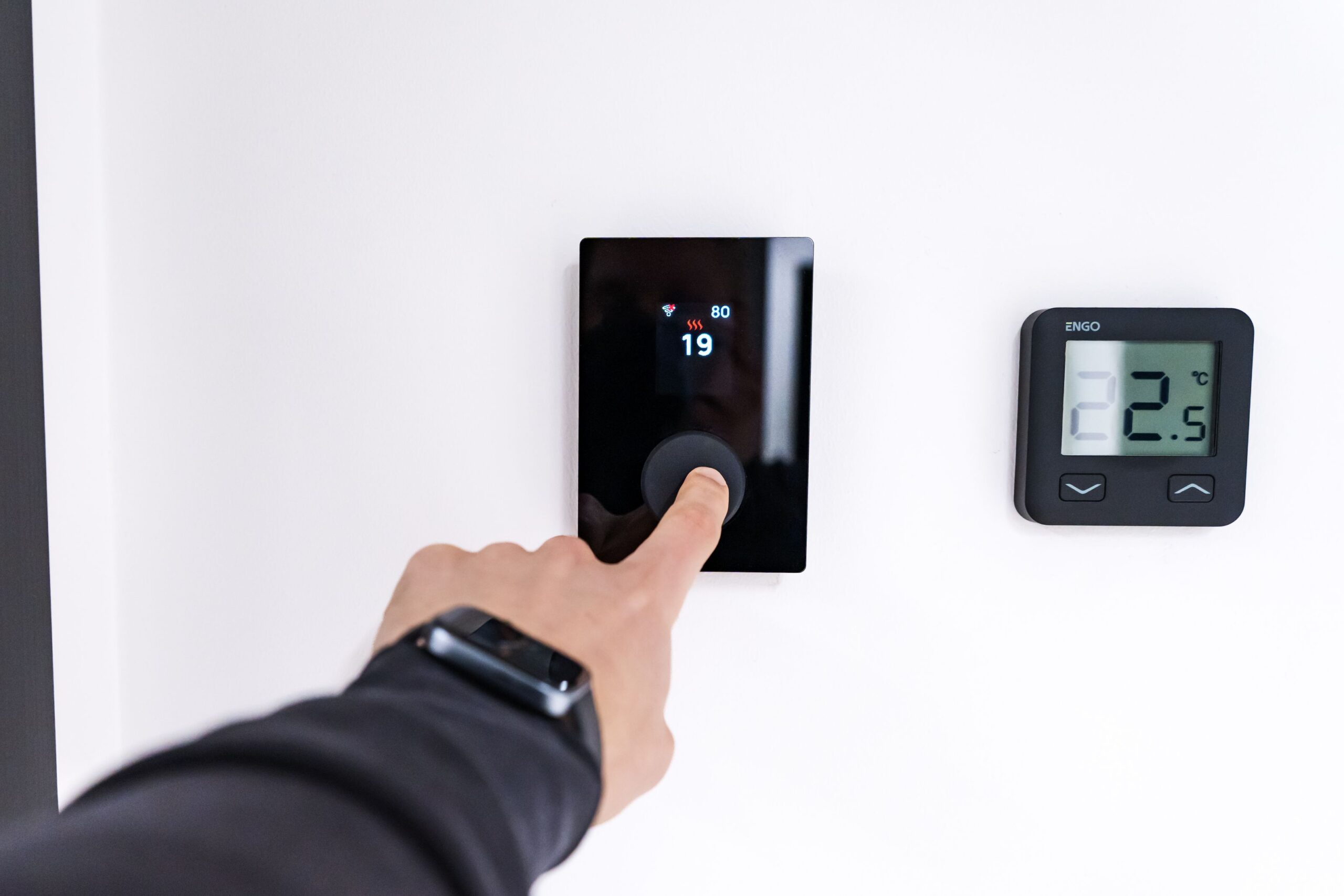 Person adjusting a modern digital smart thermostat mounted on a white wall