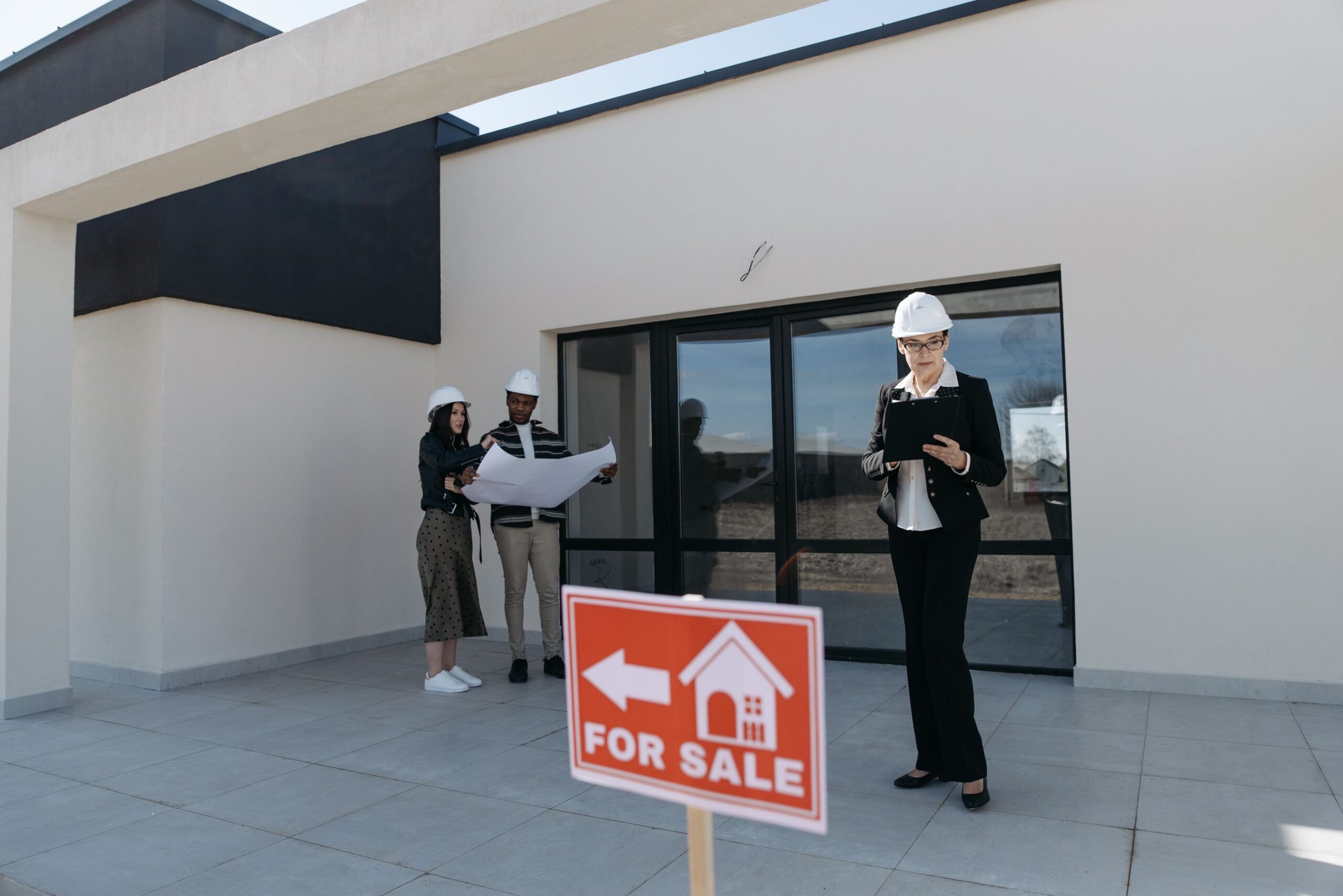 General contractor and clients in hard hats reviewing project plans outside a home before a remodel