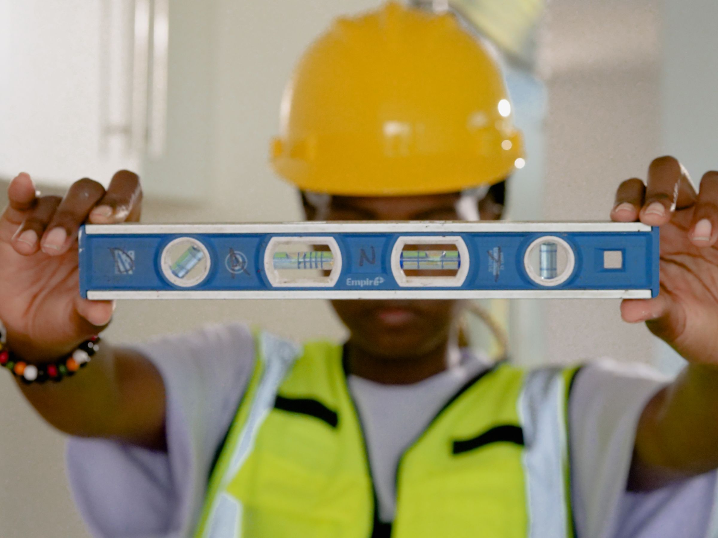 Construction worker in a yellow hard hat holding up a spirit level to check a wall on a job