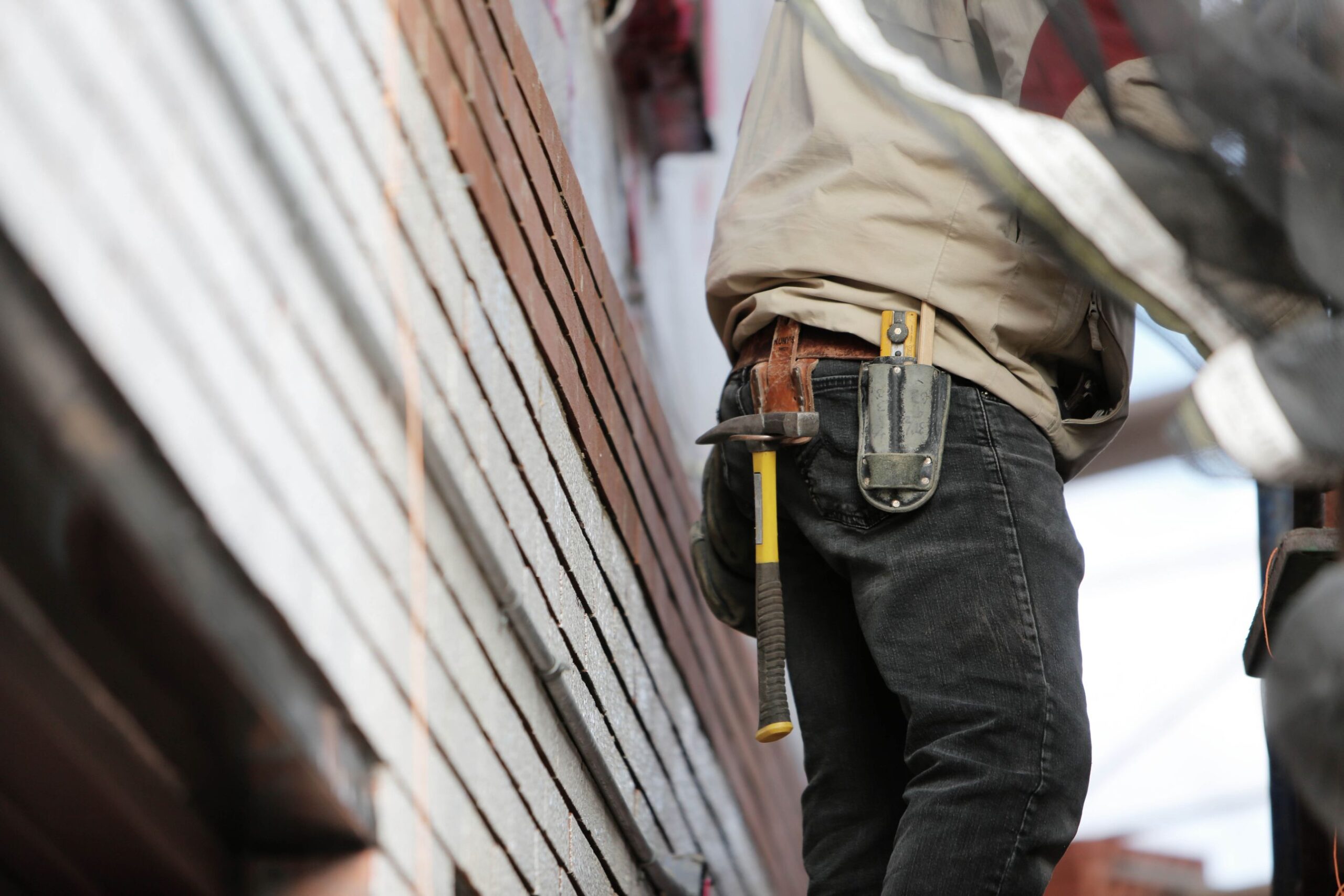 Contractor with a hammer in a leather tool belt working beside a brick wall on a renovation