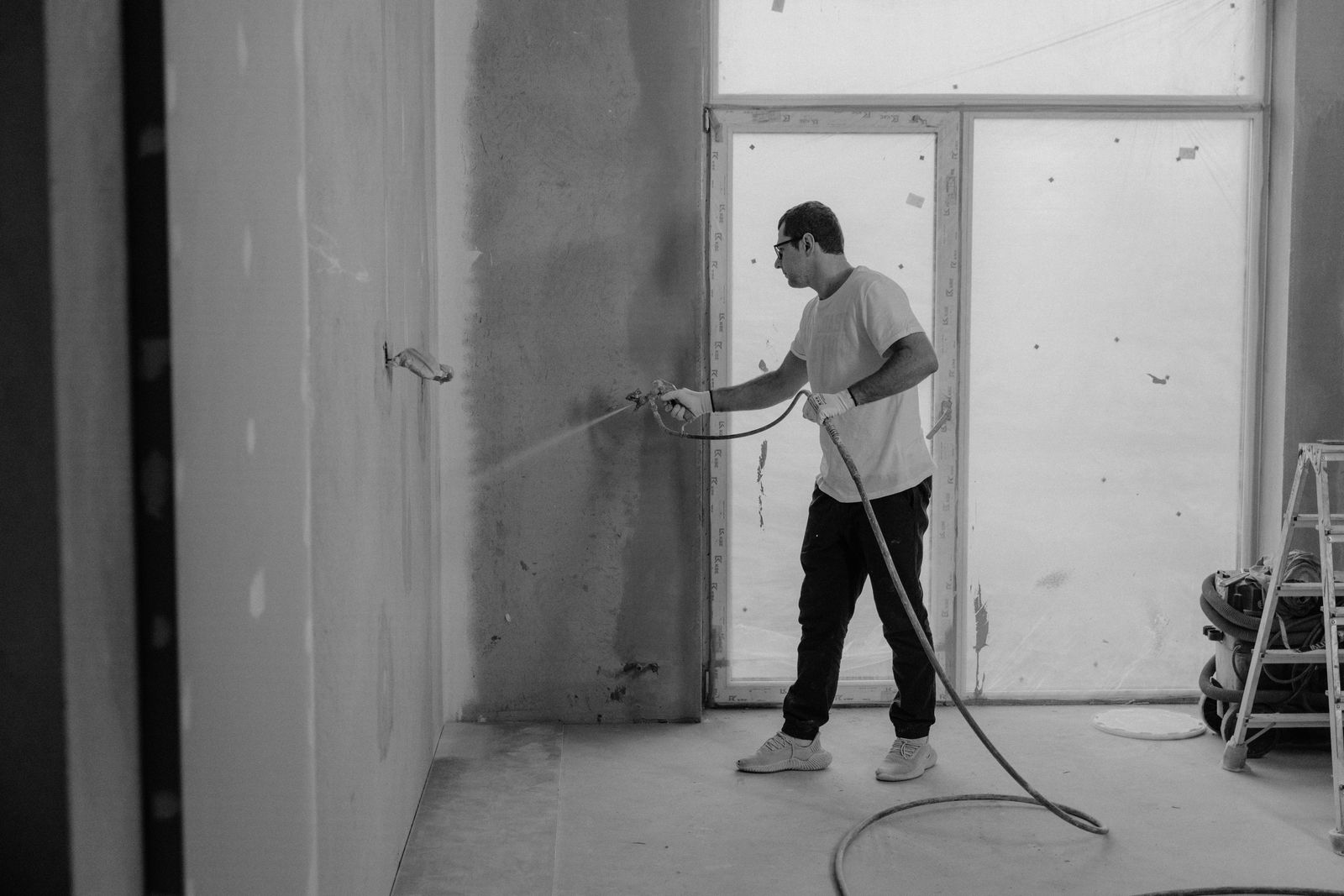 Worker using a spray gun to paint an interior wall during a residential renovation project