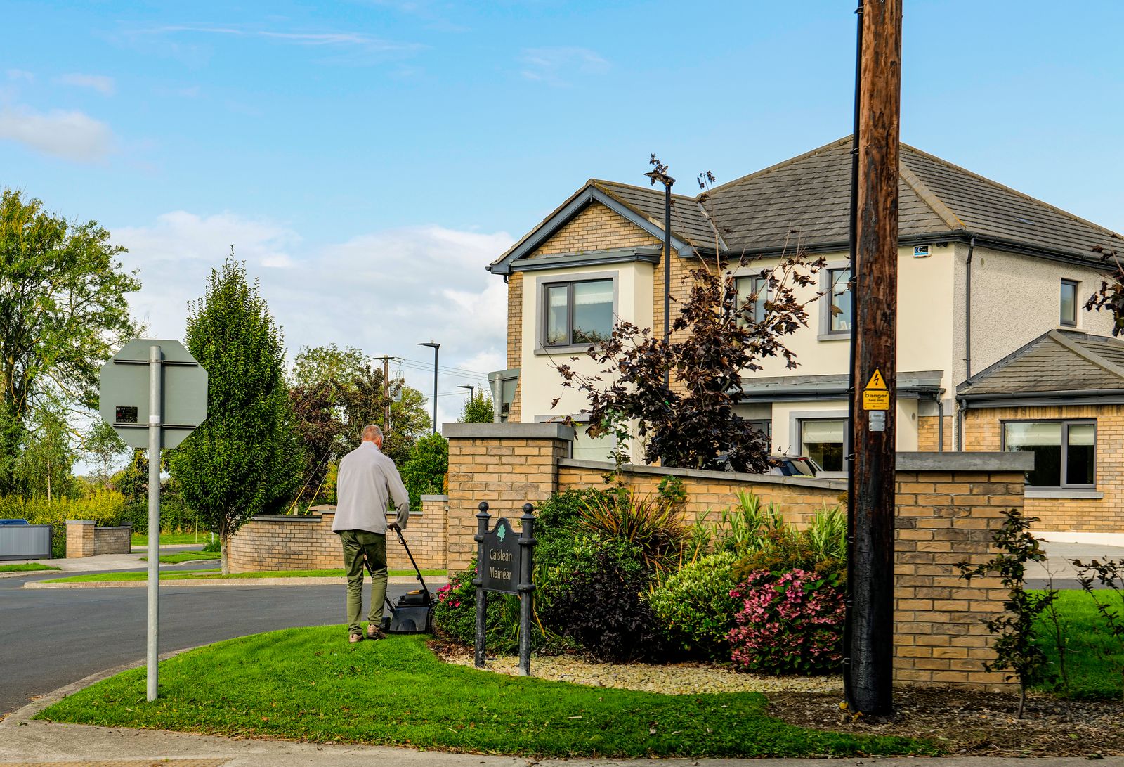A landscaper mowing the lawn outside a suburban home — the residential client landscape