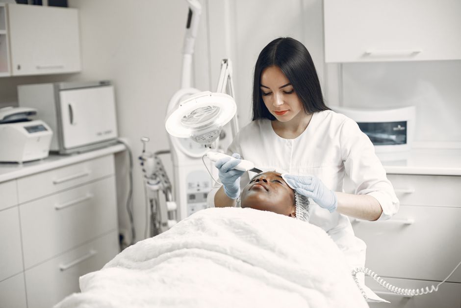 Medical aesthetician examining a patient's skin under a magnification lamp during a facial assessment