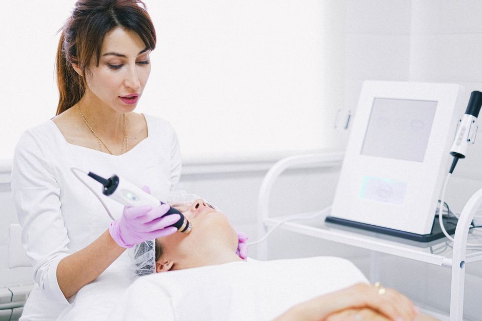 Aesthetician performing a laser facial treatment on a relaxed patient in a clean clinical environment