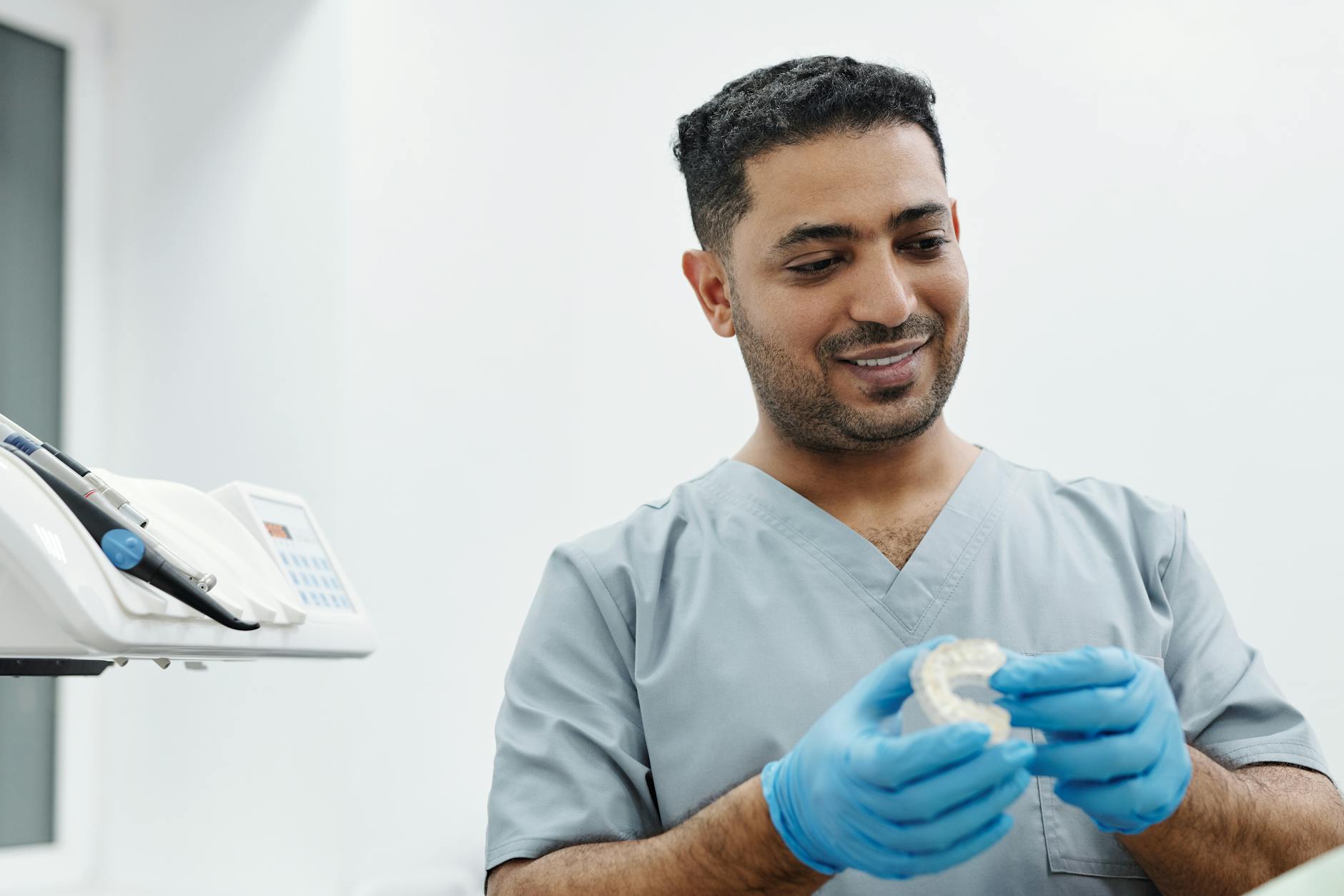 Orthodontist in scrubs holding clear aligner trays in gloved hands