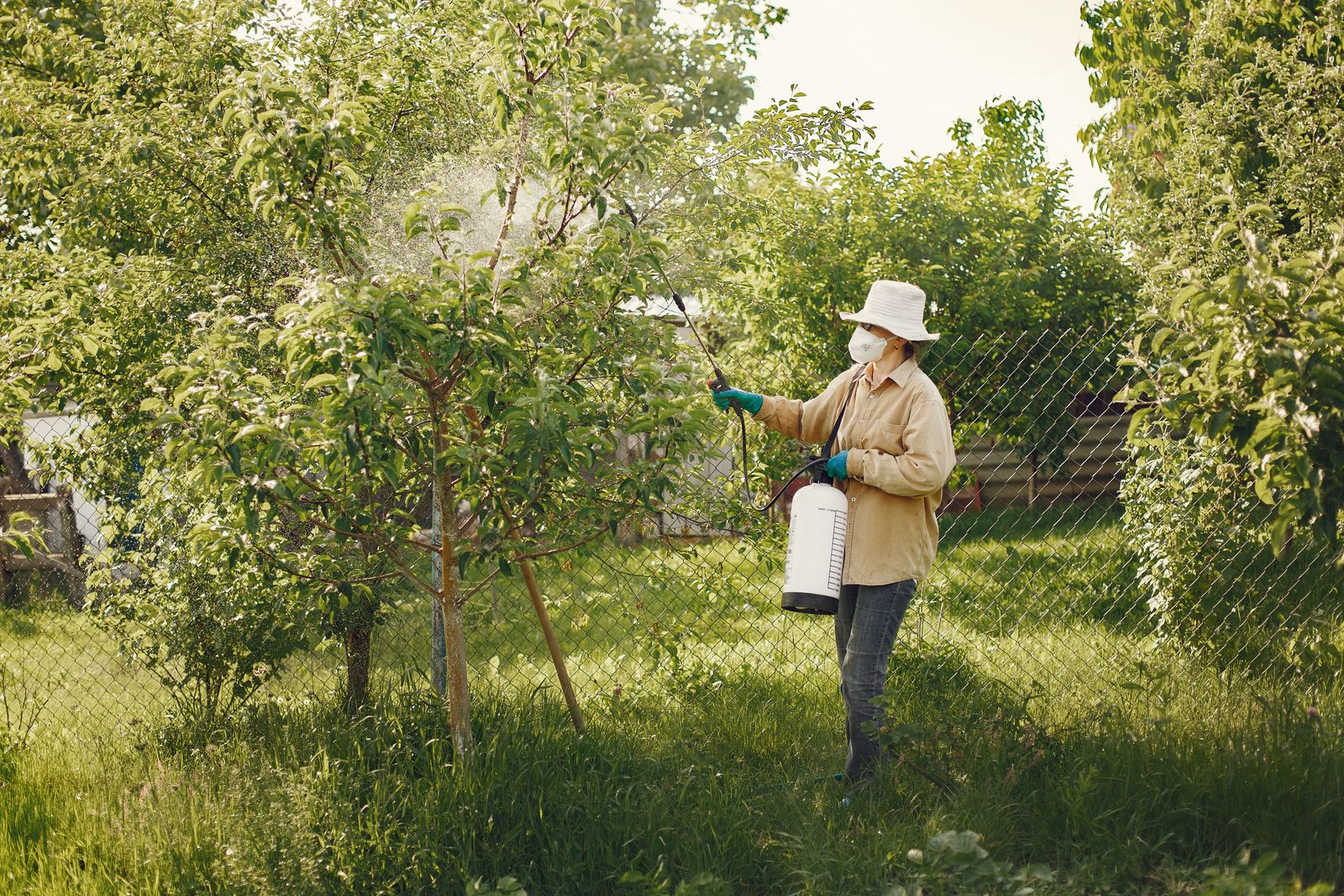 Technician in protective gear spraying for pests in a green outdoor yard