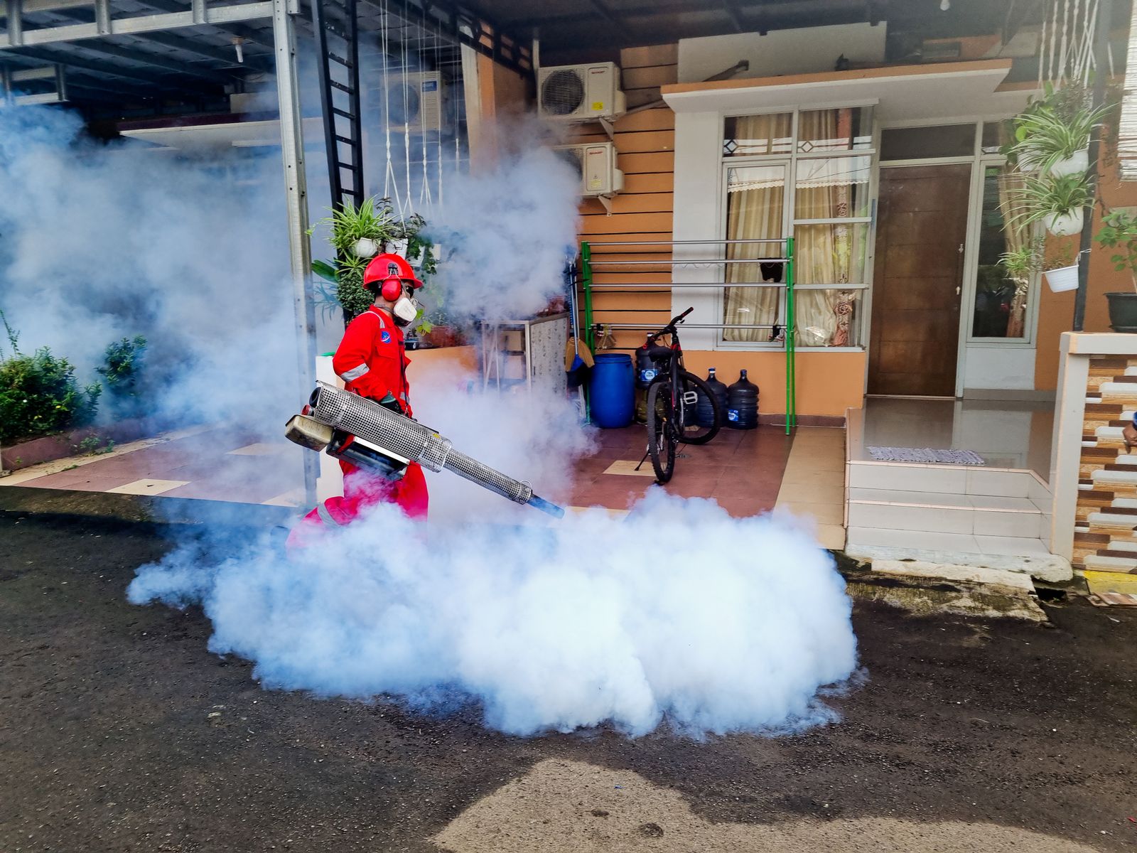 Pest control technician in red coveralls fogging the exterior of a residential home