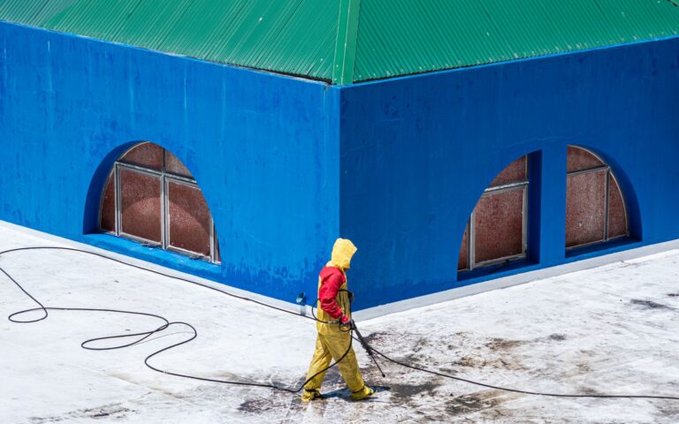 Worker in protective gear pressure washing the exterior wall of a blue commercial building