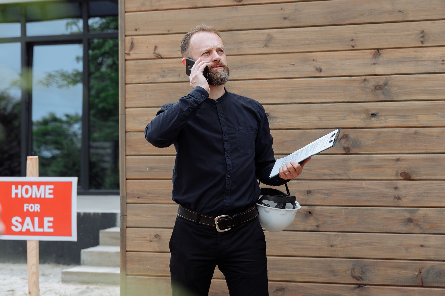 Real estate agent taking a phone call near a home for sale sign