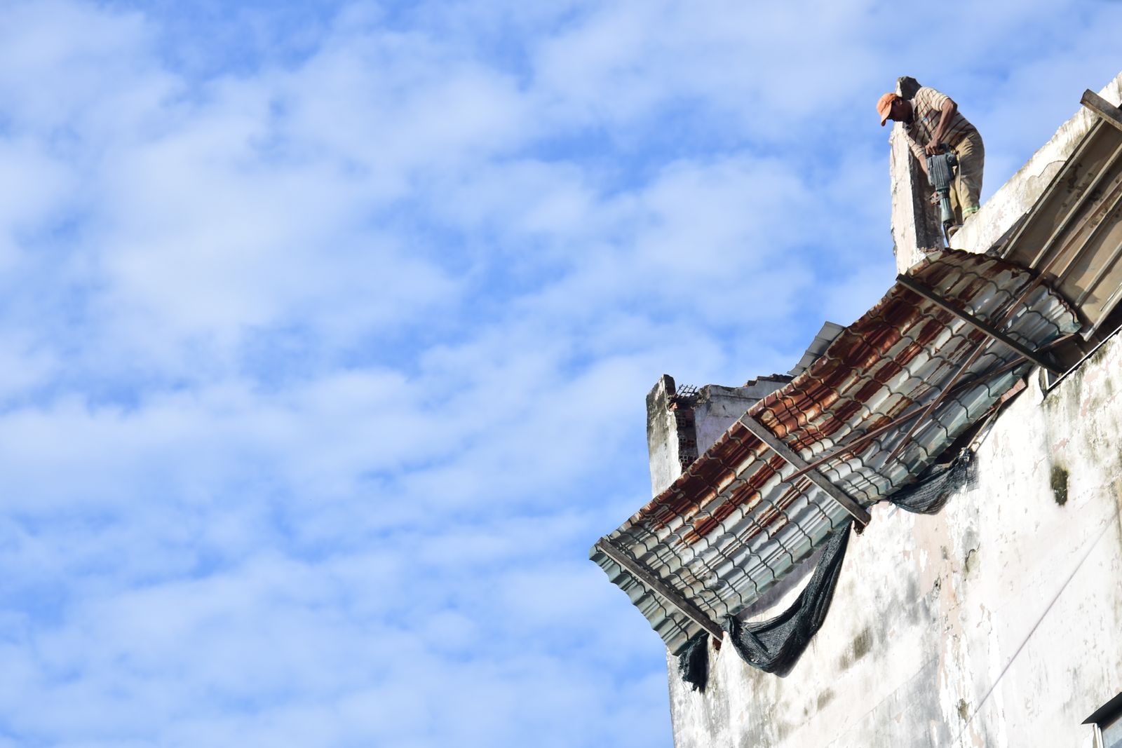 Roofer inspecting and repairing storm damage on a rooftop against a blue sky