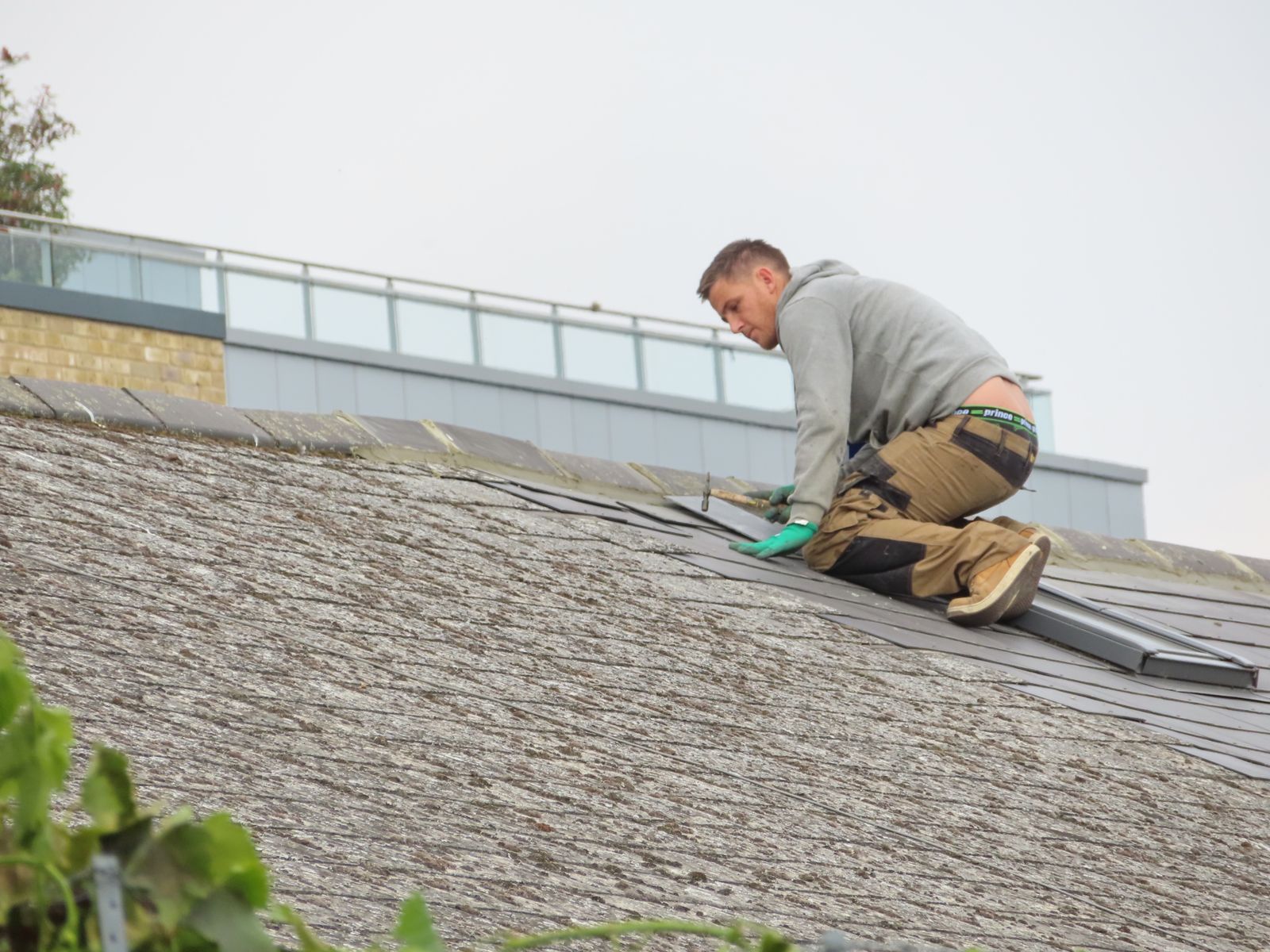 Roofing technician kneeling to replace worn shingles on a residential roof