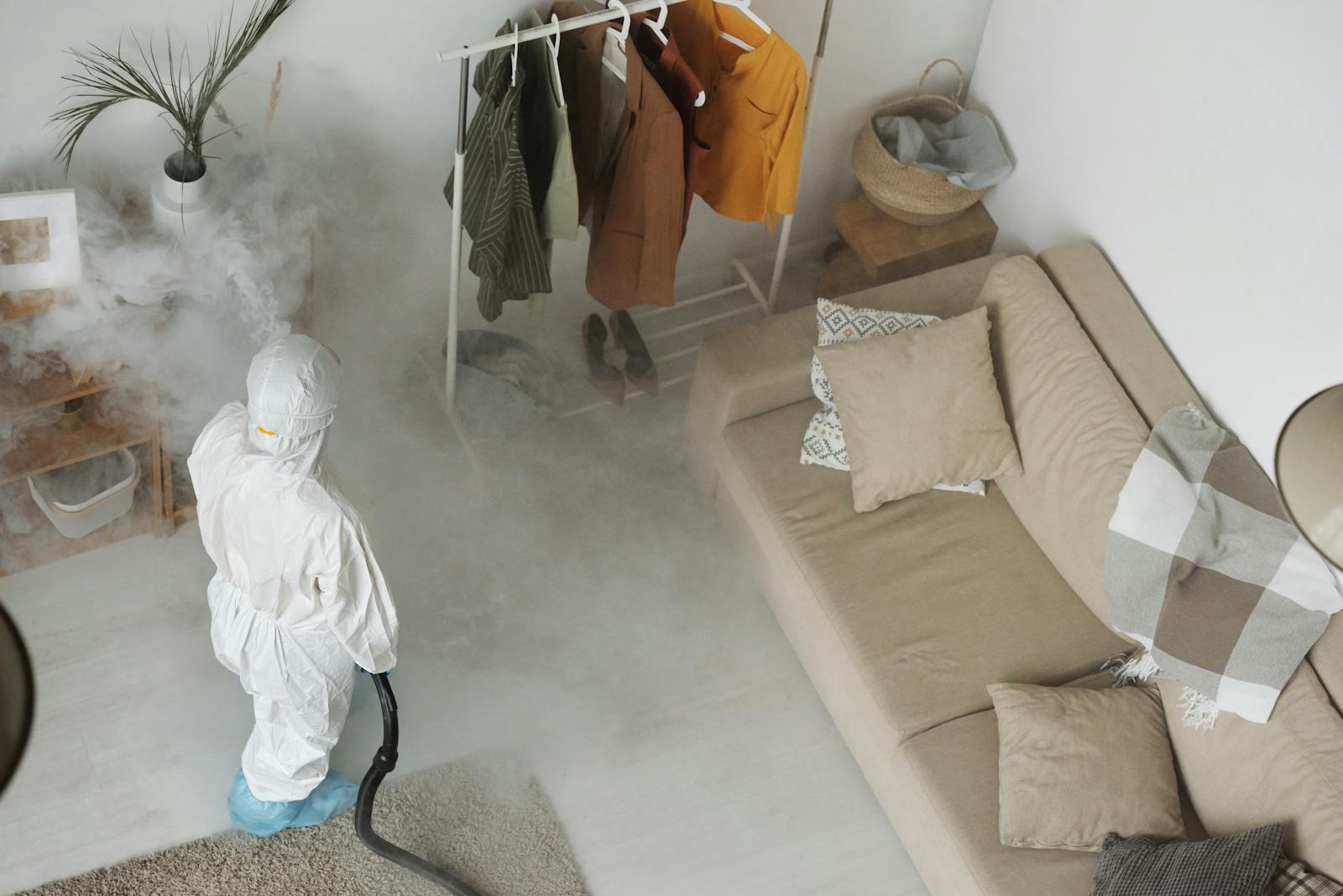 Technician in white protective suit fumigating an interior living space with smoke treatment