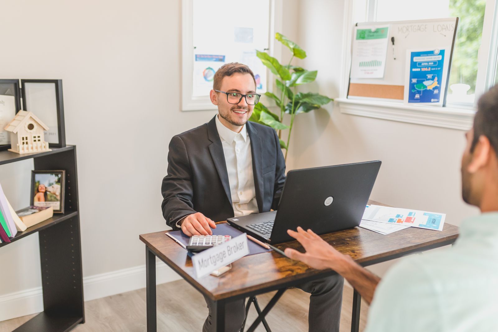 Mortgage broker meeting with a client at a desk with a Mortgage Broker nameplate