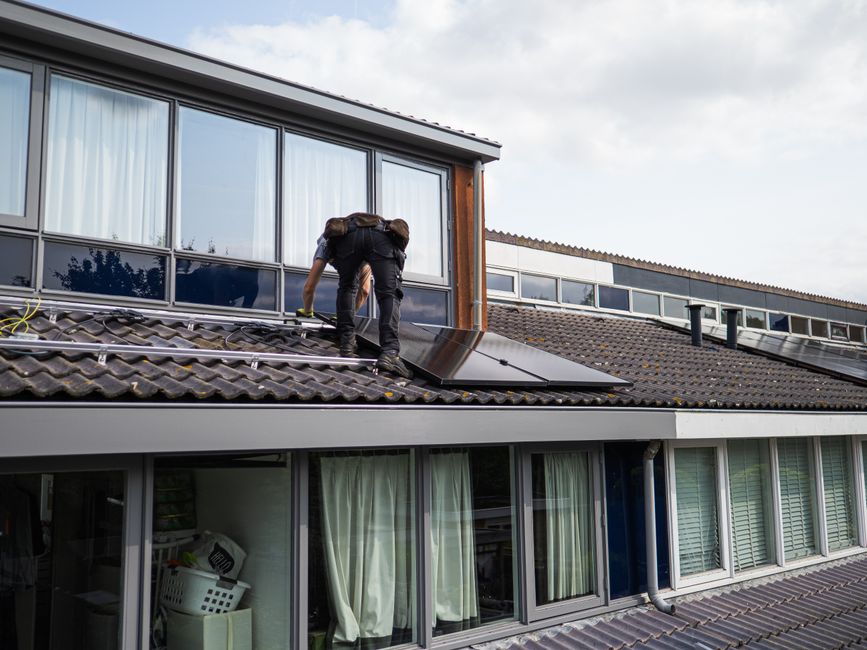 Solar technician fitting panels onto a residential tile roof on a partly cloudy day