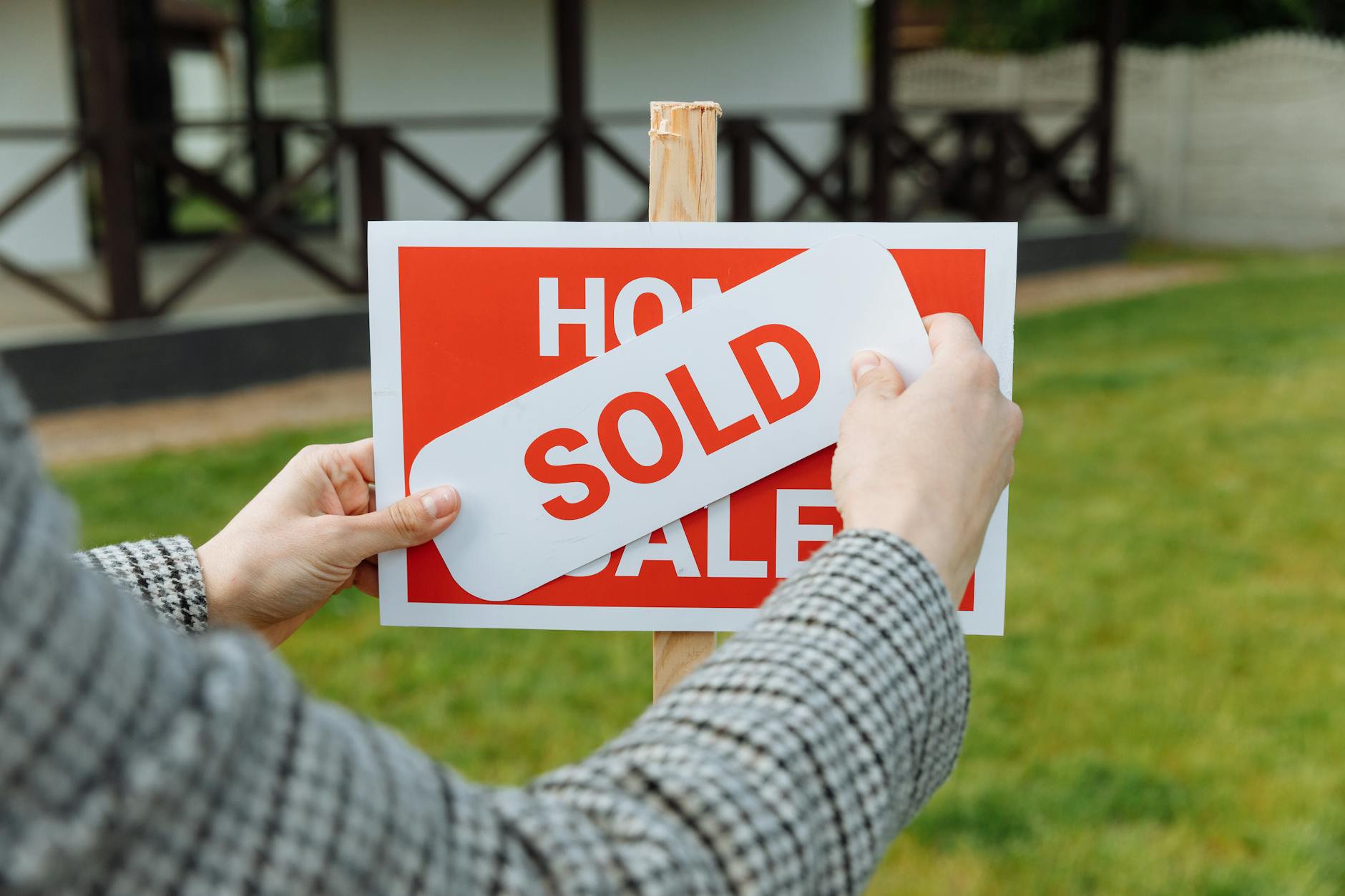 Hands placing a SOLD sticker on a red home for sale sign