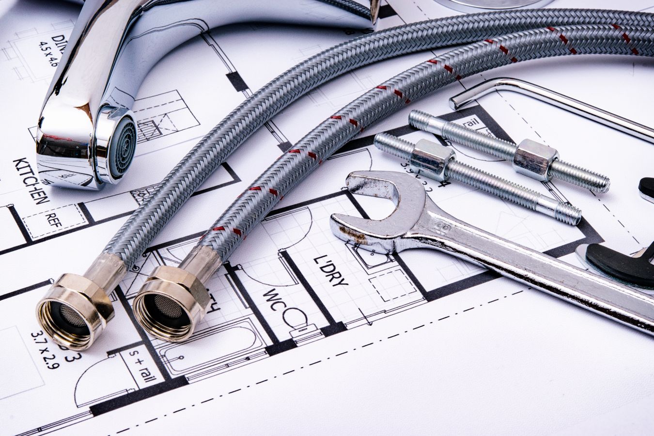 Plumbing tools and chrome supply lines arranged on architectural blueprints