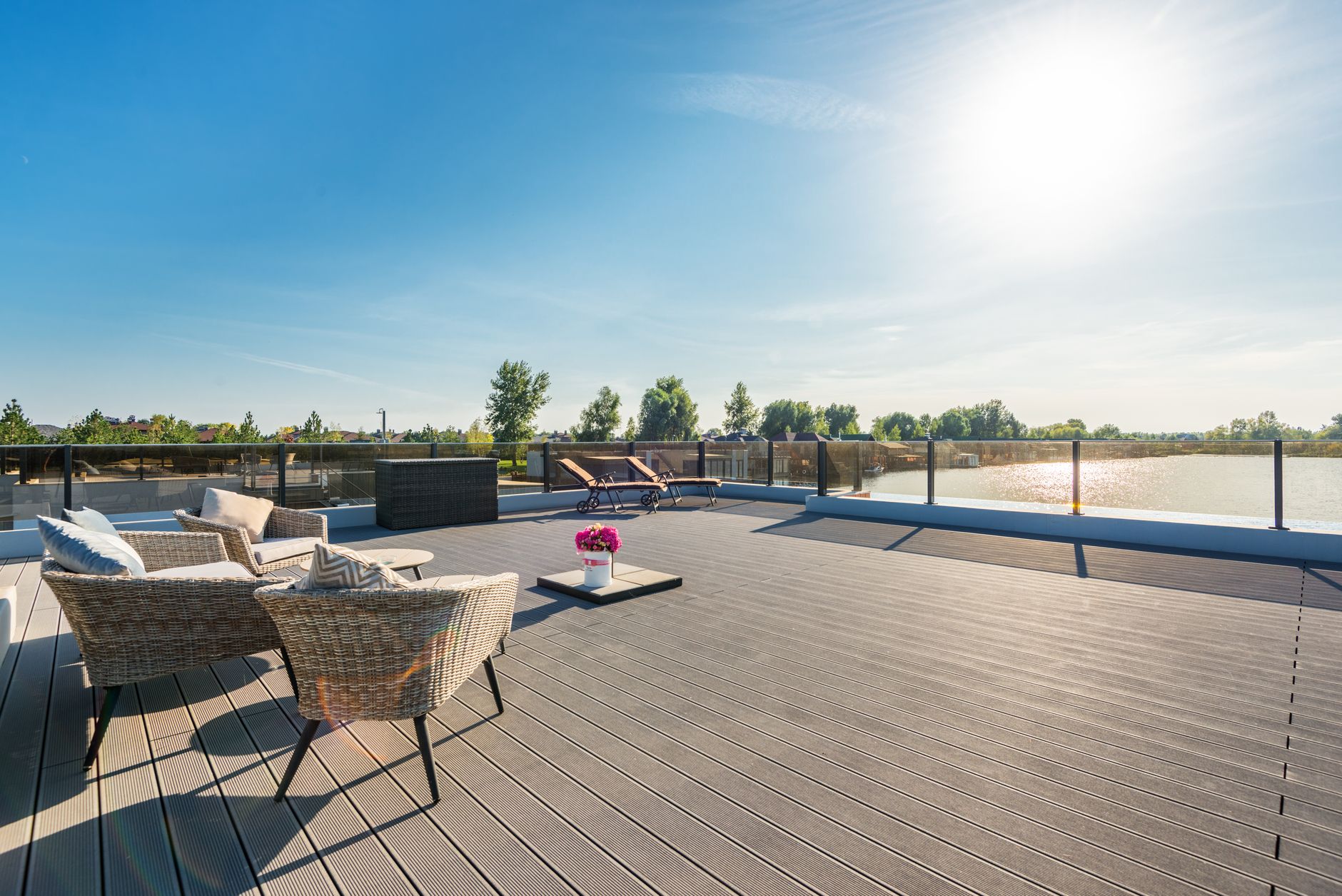 Large composite deck with wicker lounge chairs and a glass railing overlooking a lake
