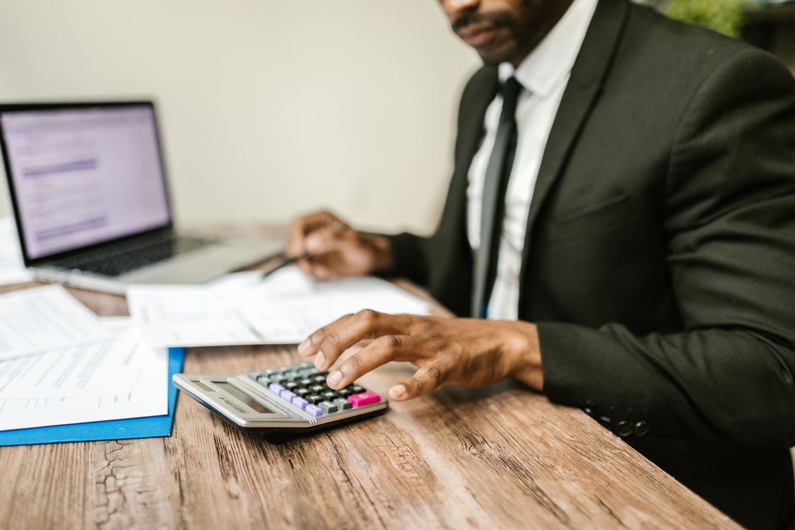 CPA using calculator with financial documents and laptop open