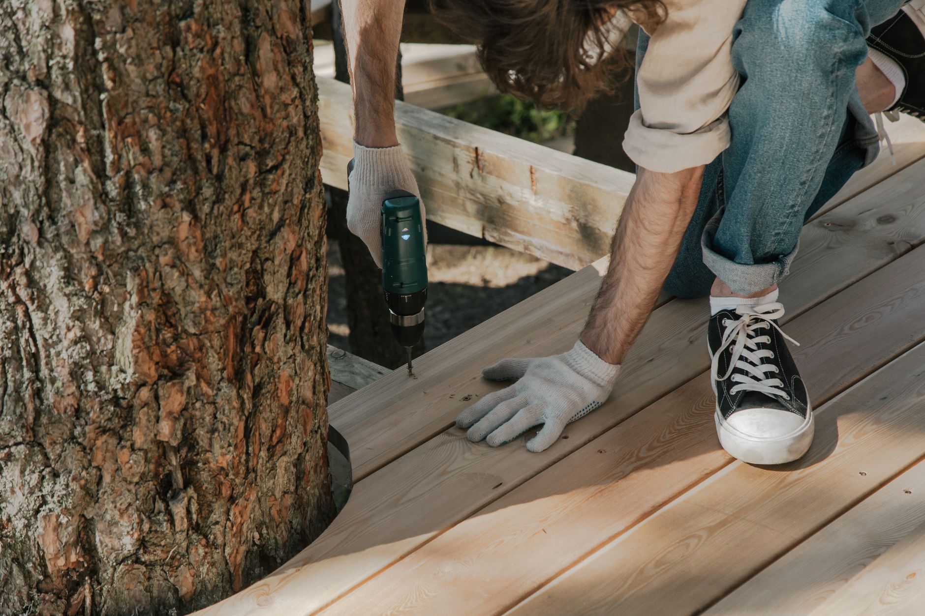 Deck builder kneeling to drive a screw into a fresh decking board with a cordless drill