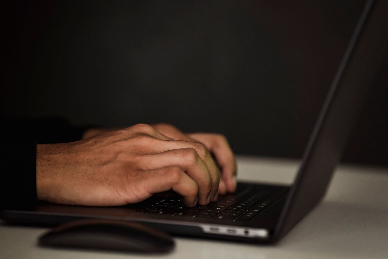 Close-up of hands typing on a dark laptop keyboard at night